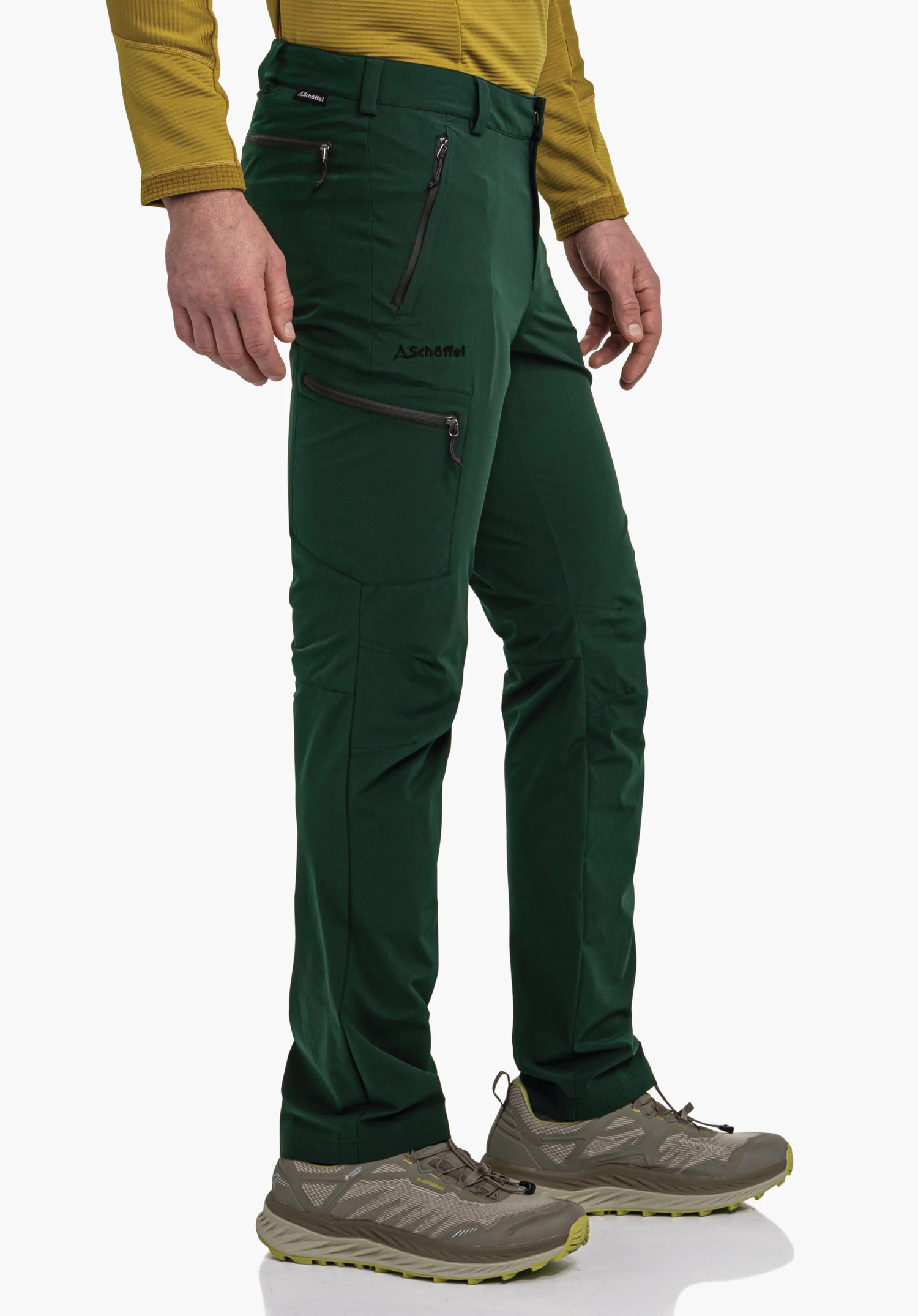 Pants Folkstone donkergroene wandelbroek met Schöffel-logo (tekst: 'Schöffel'), gedragen; met ritszakken, staande man in lichtgeel shirt met lange mouwen en wandelschoenen voor een witte achtergrond.
