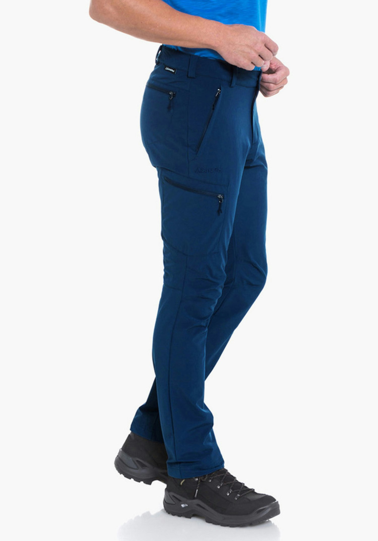 Pants Folkstone man in a light blue T-shirt poses side-on with hands on belt, wears dark blue hiking trousers and black hiking boots, neutral white background, smiling and looking right.