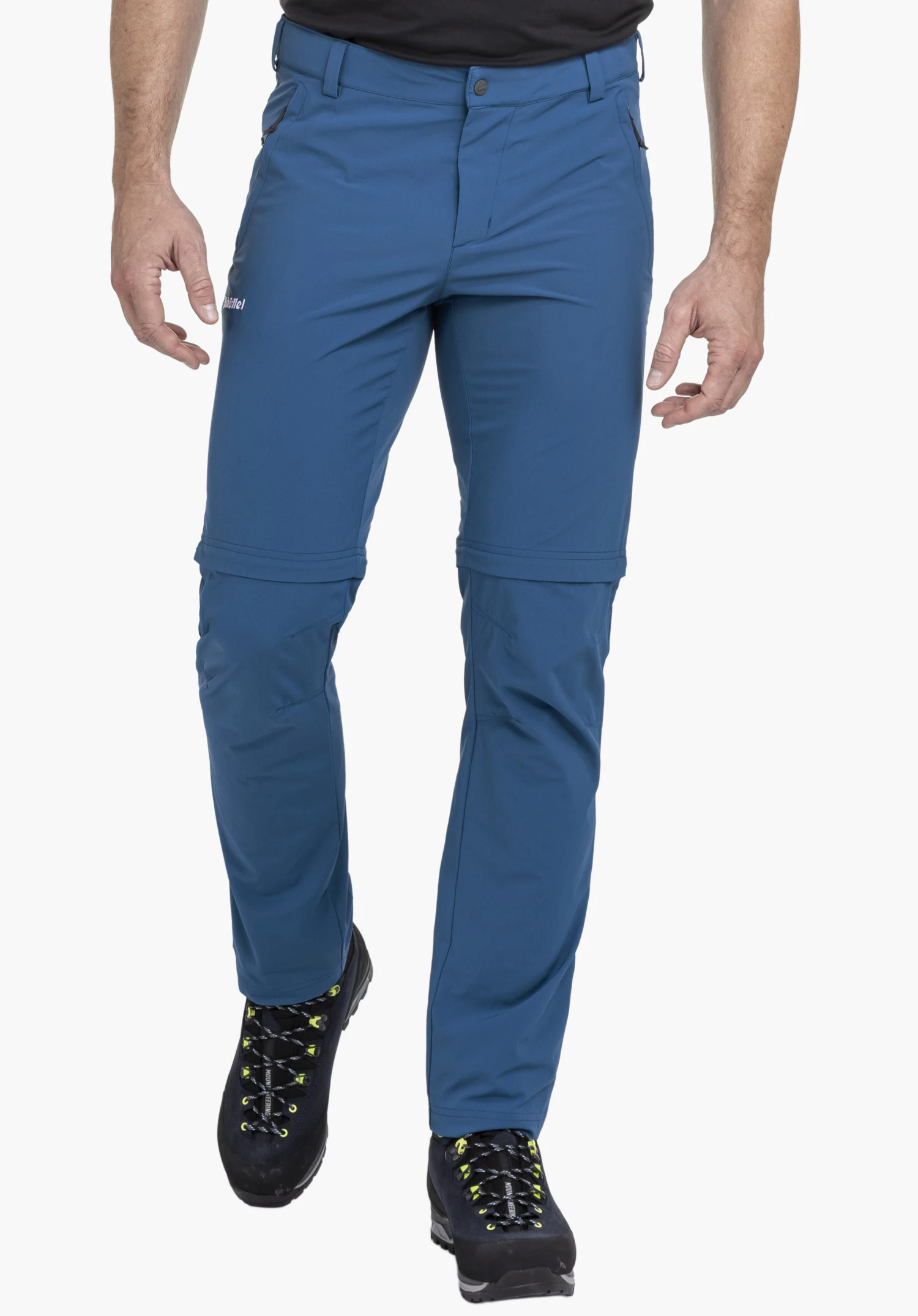 Pants Folkstone Zip Off. Een model draagt de blauwe broek en staat frontaal met één been iets naar voren geplaatst. Het witte Schöffel-logo is duidelijk zichtbaar op het rechterbovenbeen, gepresenteerd tegen een neutrale achtergrond.