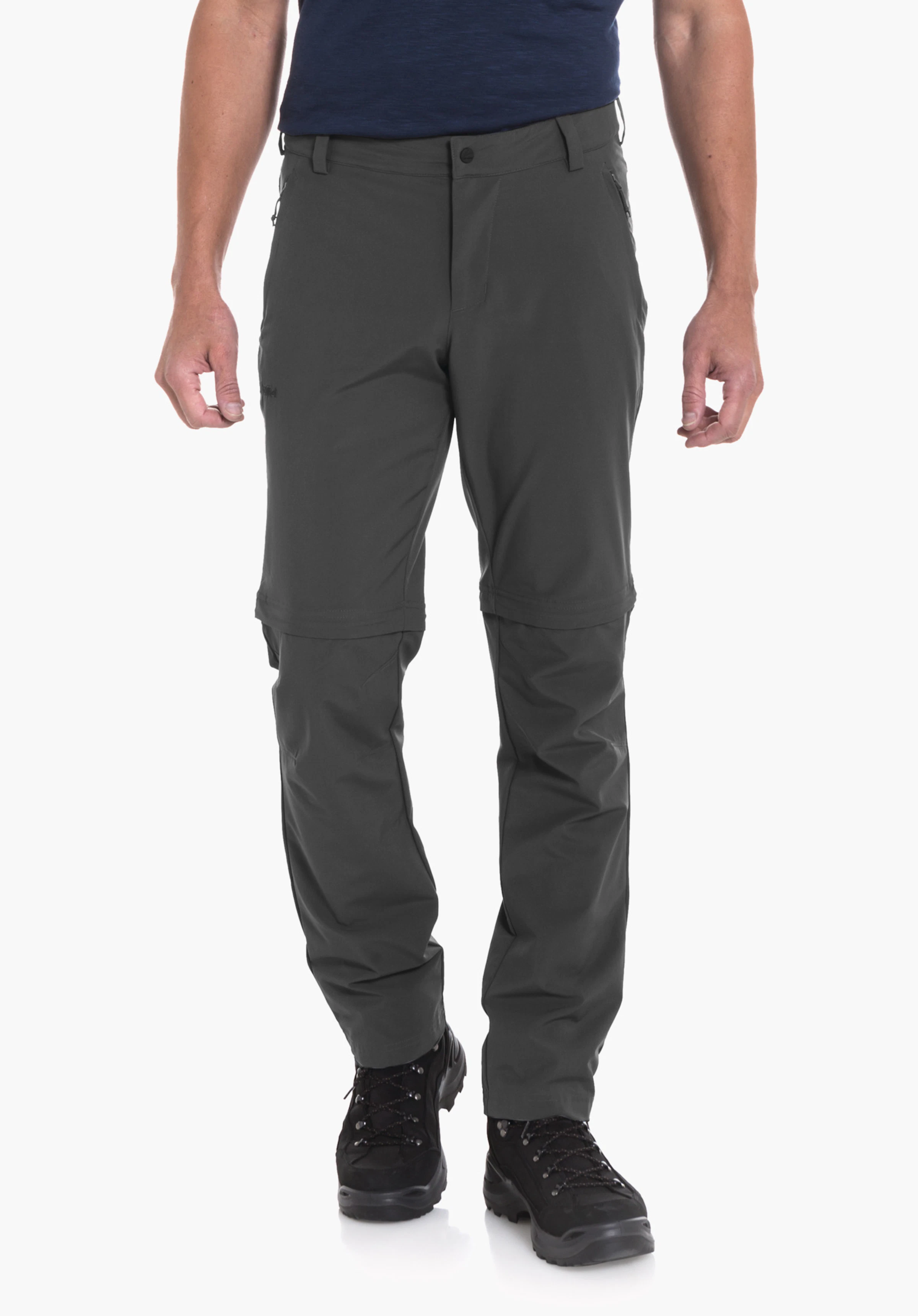 Pants Folkstone Zip Off Mann steht frontal, trägt ein dunkelblaues T‑Shirt mit Bergmotiv und dunkelgrüne Zip-off-Hose, blickt zur Seite vor hellem Hintergrund. Text auf Shirt: "A. Schöffel".