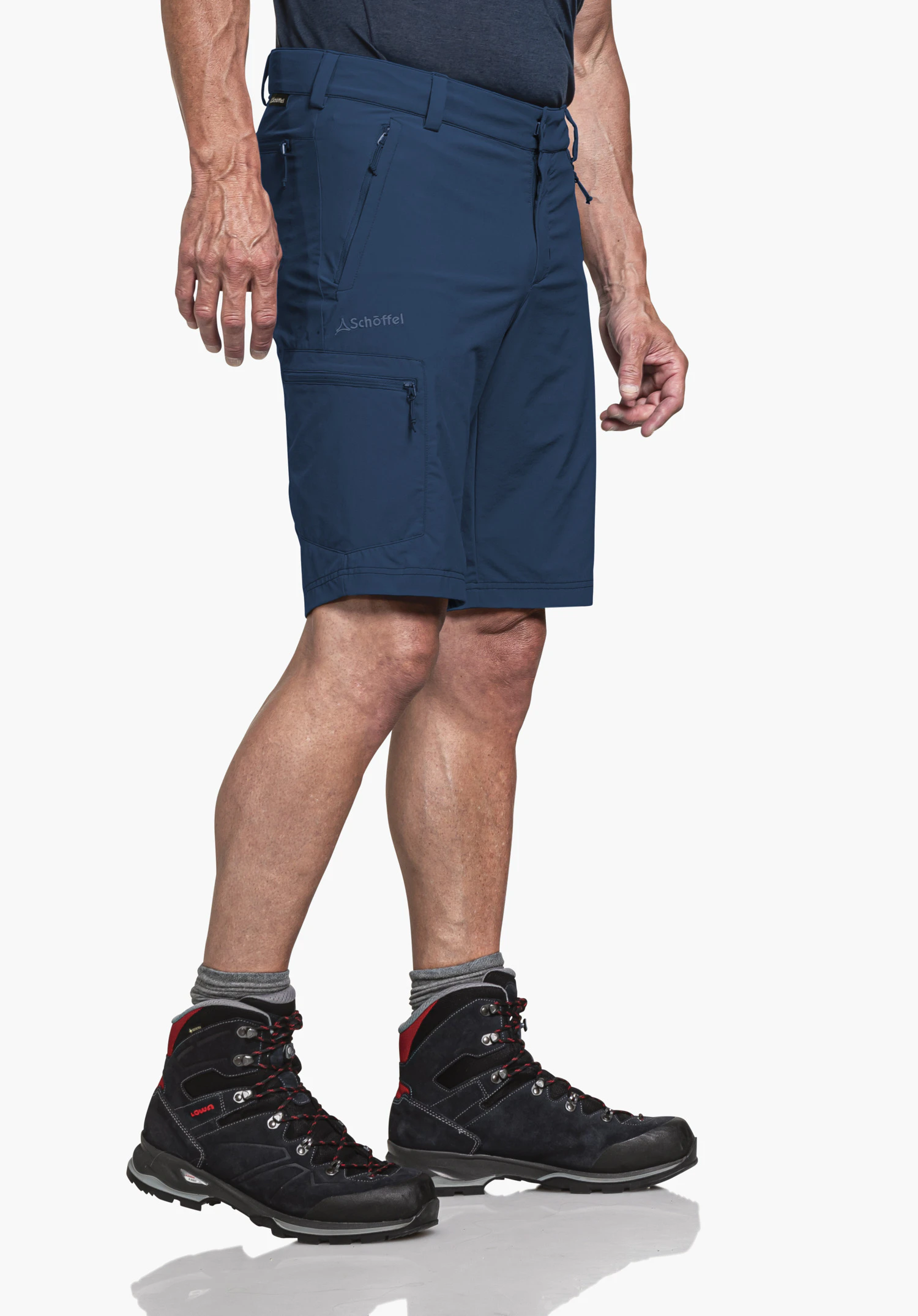 Shorts Folkstone in het blauw, getoond op een model in zijaanzicht voor een neutrale achtergrond. Het subtiele Schöffel-logo op de rechterbroekspijp benadrukt de functionele uitstraling voor outdoor-avonturen.