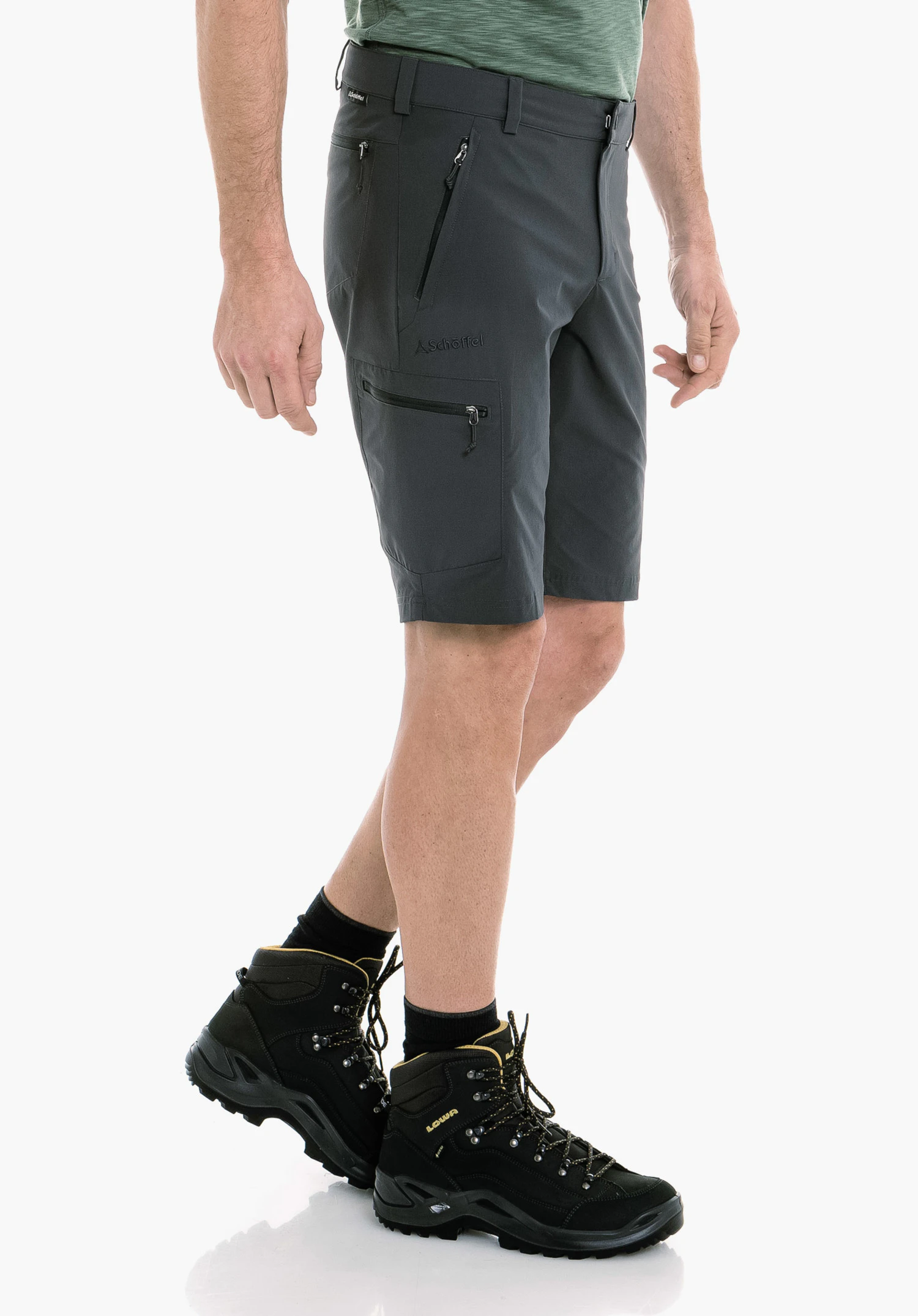 Shorts Folkstone in Grau: Der männliche Wanderer steht in einer seitlichen Pose vor einem neutralen Hintergrund. Die Hose präsentiert sich in funktionalem Design mit einem dezenten Schöffel-Logo am Oberschenkel, ideal für anspruchsvolle Outdoor-Abenteuer.