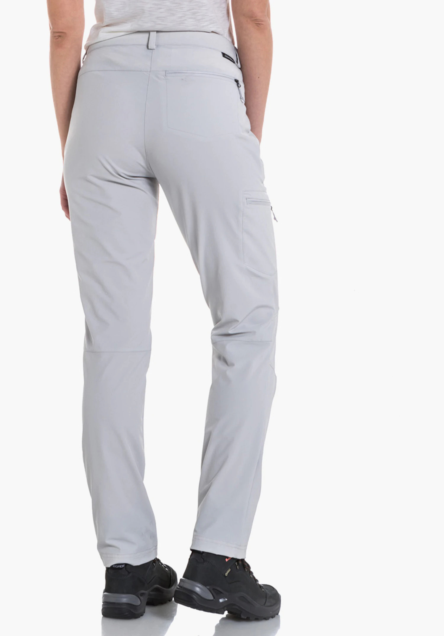Pants Ascona femme portant un pantalon gris clair, debout dos à la caméra, mains dans les poches; t-shirt blanc et chaussures noires, fond blanc neutre.