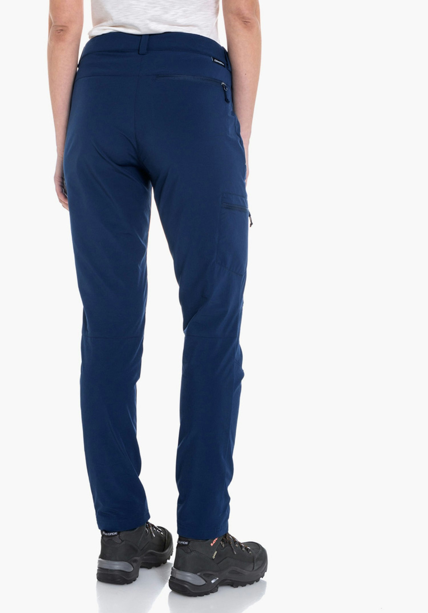 Pants Ascona pantalon bleu foncé, porté par une femme en vue arrière, combiné avec t-shirt blanc clair et chaussures noires devant un fond blanc lumineux.