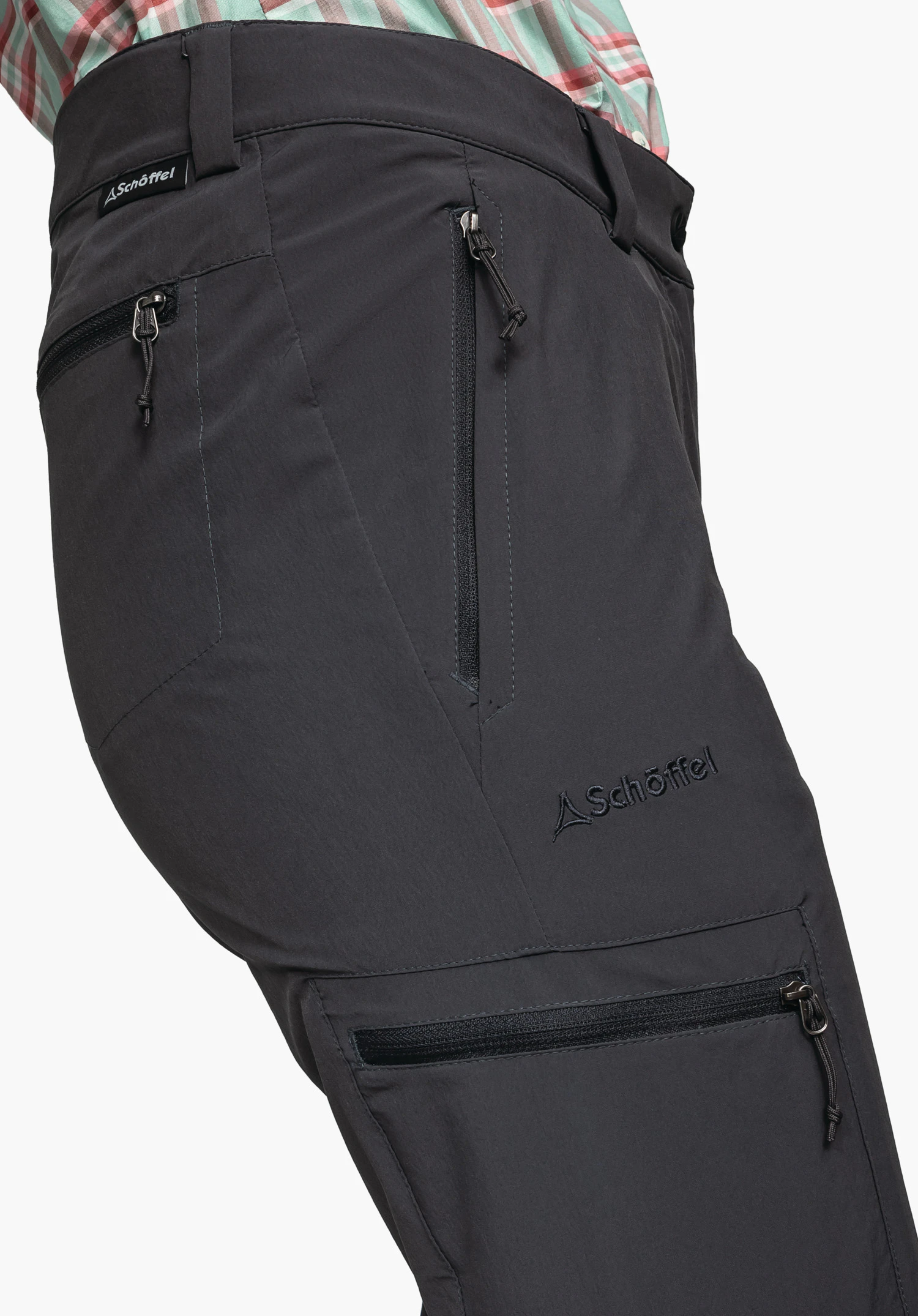 Pants Ascona, the embroidered Schöffel logo on the thigh as well as the zip pockets at the waist and on the leg in grey, close-up against a white/neutral background.