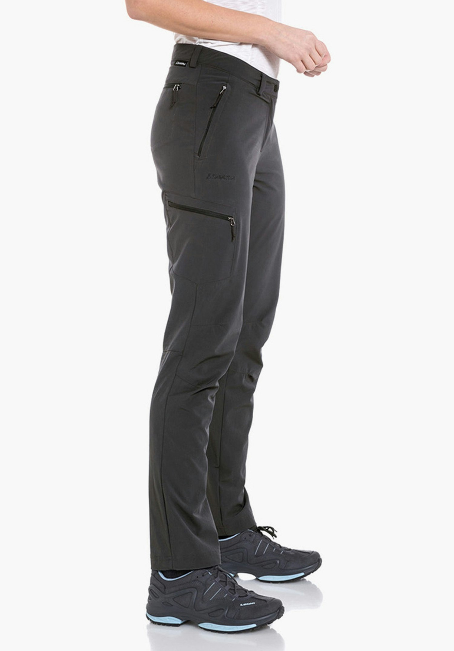 Pants Ascona Frau trägt hellgrünes kariertes Hemd mit rot-weißem Muster, steht seitlich, Hand in Tasche einer dunkelgrauen Outdoorhose, hellgraue Wanderschuhe, weißer Hintergrund.