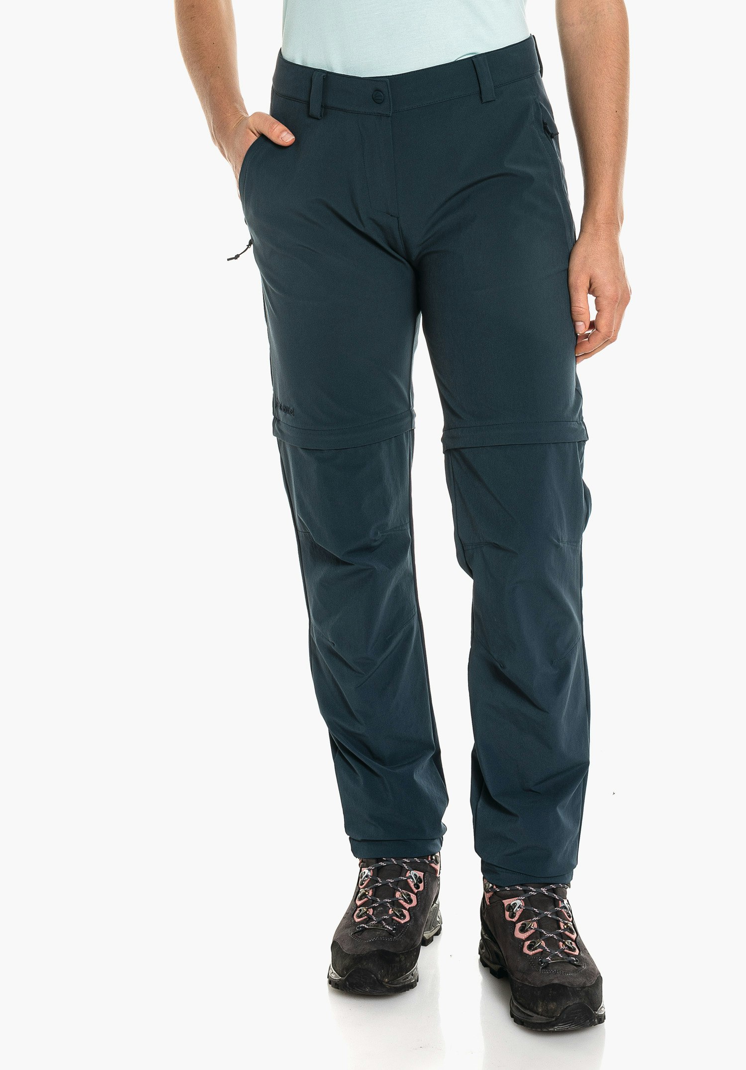 Pants Ascona Zip Off dark blue zip-off trousers worn by a standing person; one hand in pocket, light blue top, black hiking shoes, neutral white studio background.