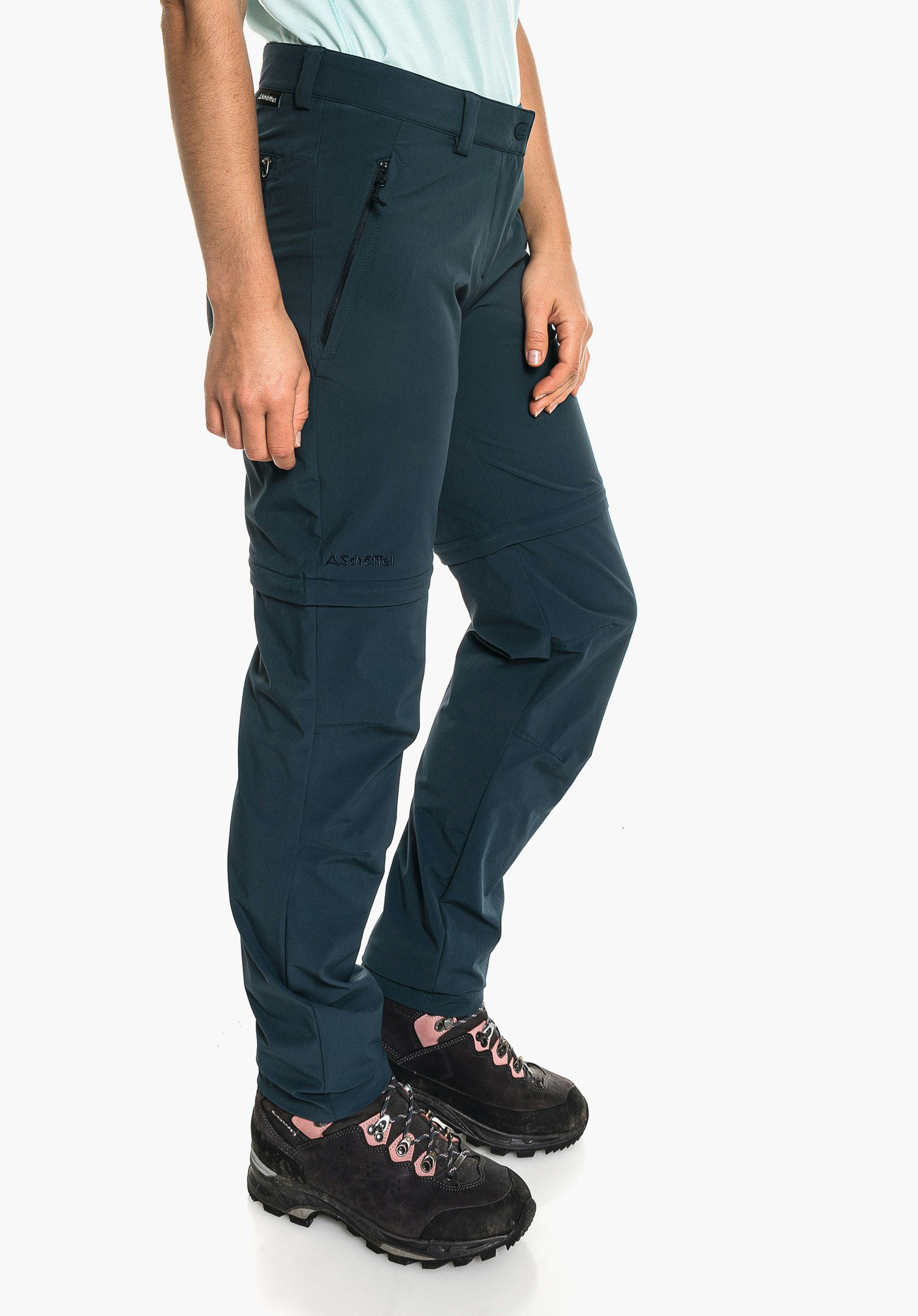 Pants Ascona Zip Off dark blue trekking trousers worn by a standing person in a relaxed pose in front of a white studio background; black hiking shoes. Text: "Schöffel".