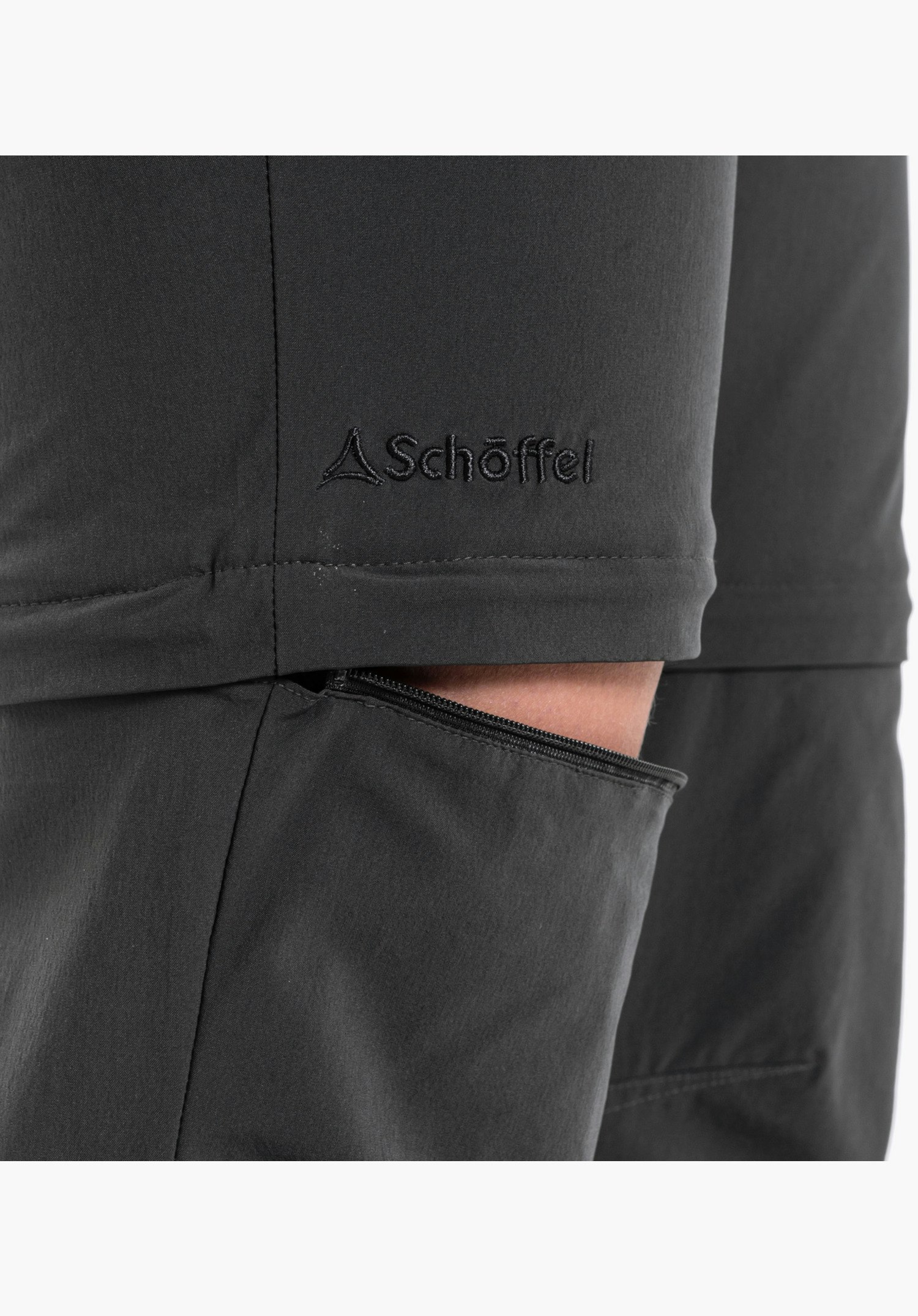 Pants Ascona Zip Off zeigt den teilweise geöffneten Reißverschluss der Zip-Off-Funktion und das gestickte Schöffel-Logo auf dem grauen Material, Nahaufnahme vor weißem/neutralem Hintergrund.