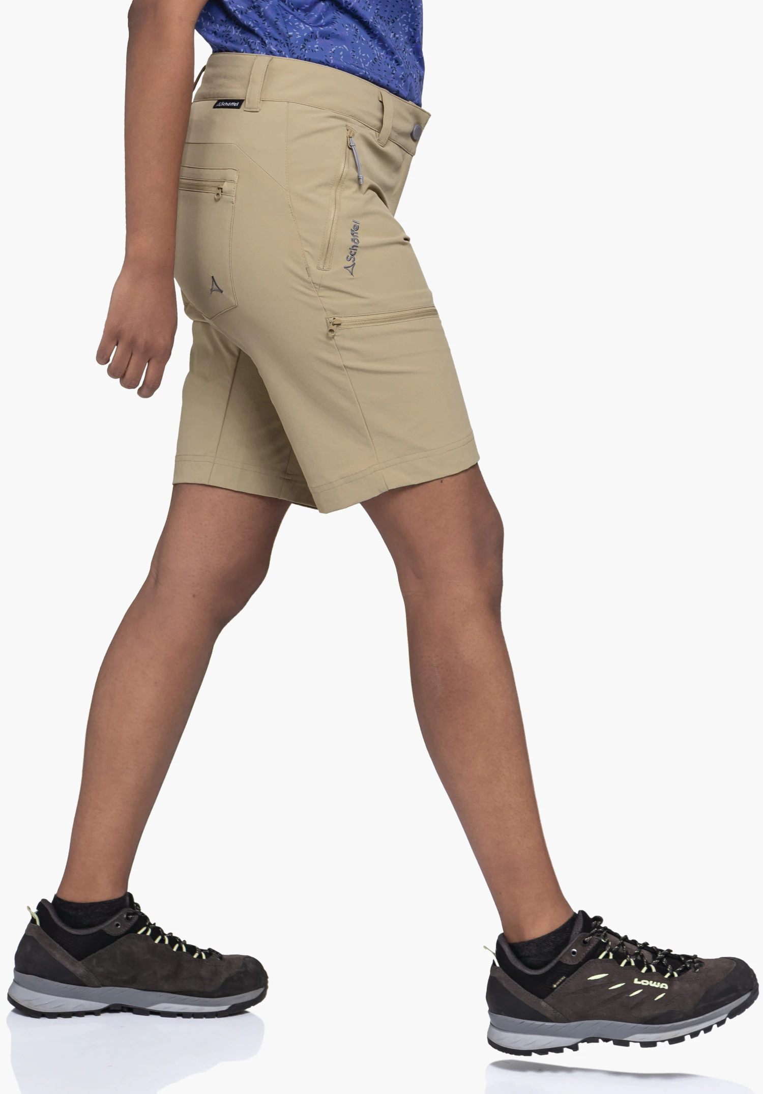 Shorts Toblach2 en beige est porté par un mannequin photographié de profil dans un mouvement de marche. Le Schöffel-Logo est visible sur le côté du pantalon. L'image est prise devant un fond neutre.