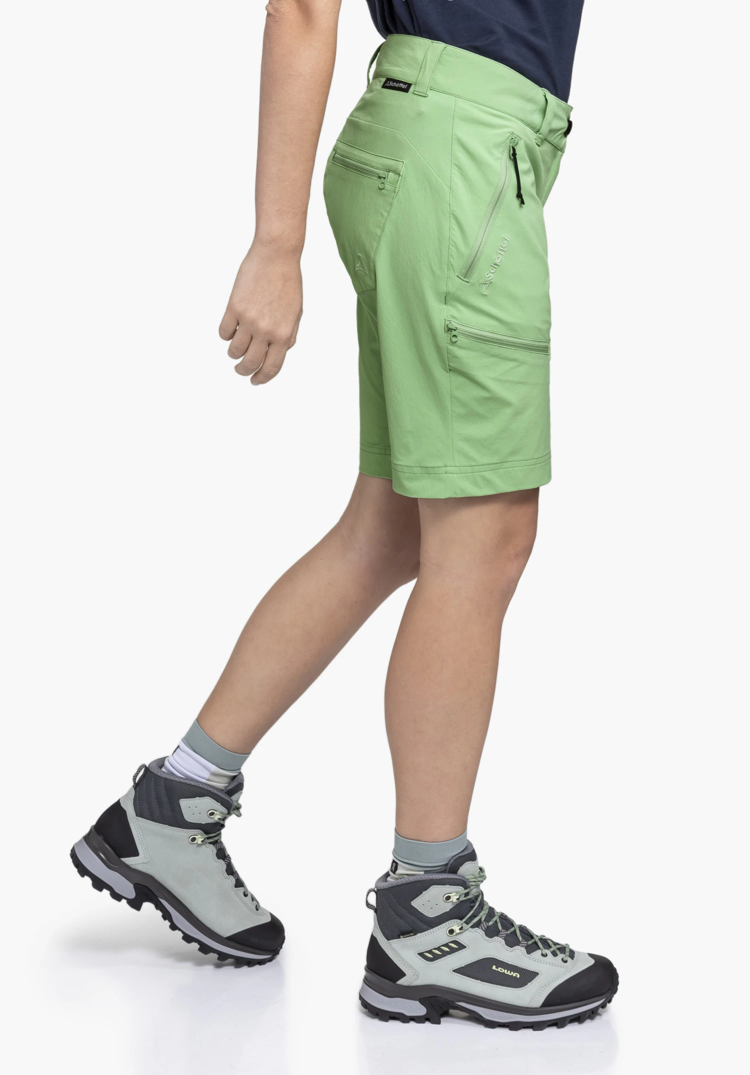 Shorts Toblach2. Een model draagt de groene korte broek en staat zijwaarts in een loopbeweging, waardoor de ritszakken en het Schöffel-Logo aan de zijkant zichtbaar worden. De draagweergave wordt gepresenteerd tegen een neutrale achtergrond.