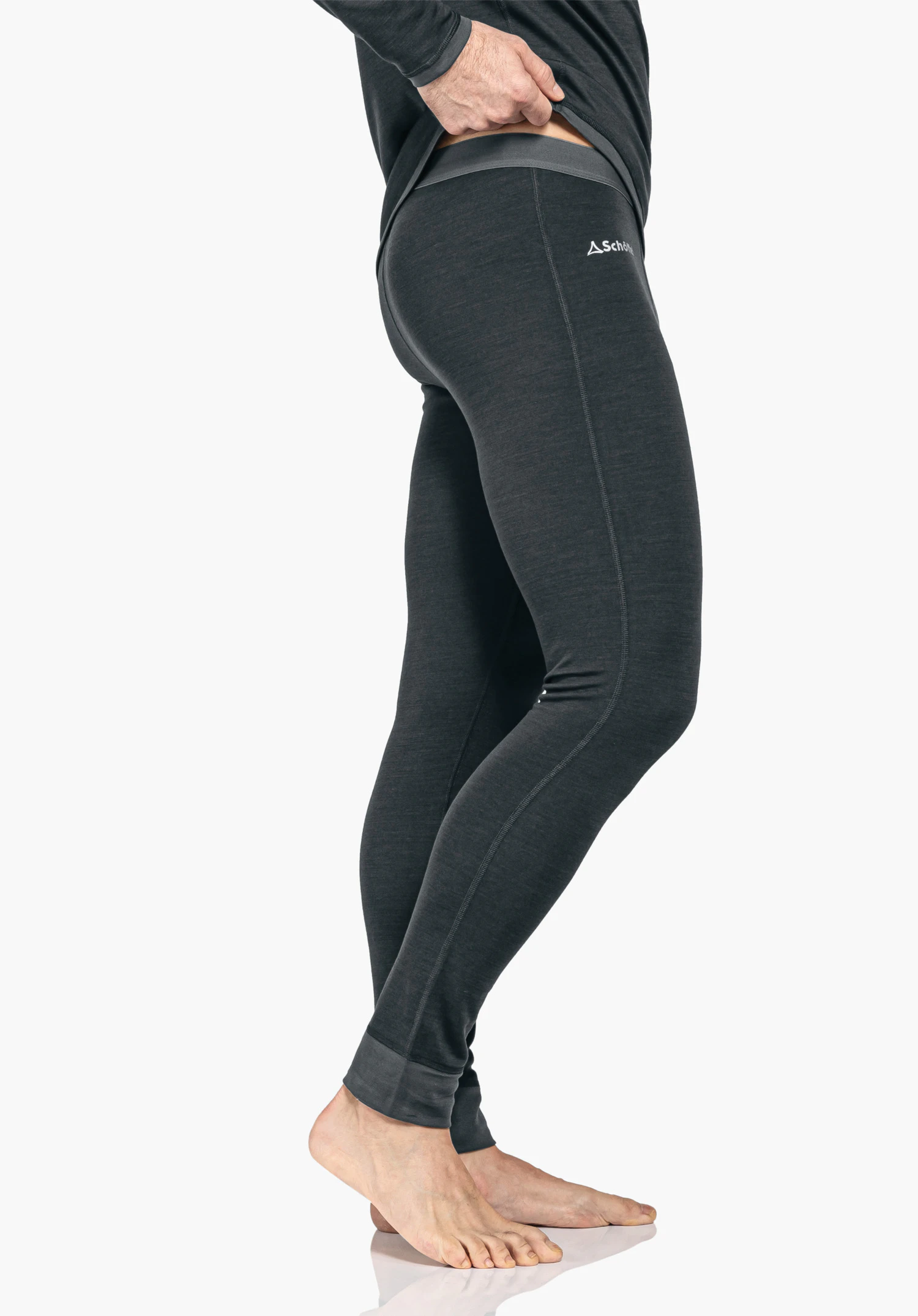 Merino Sport Pants long M dark grey functional leggings, person slightly lifts the waistband; standing side view in front of a light neutral background. Text: "Schöffel". Schöffel logo.