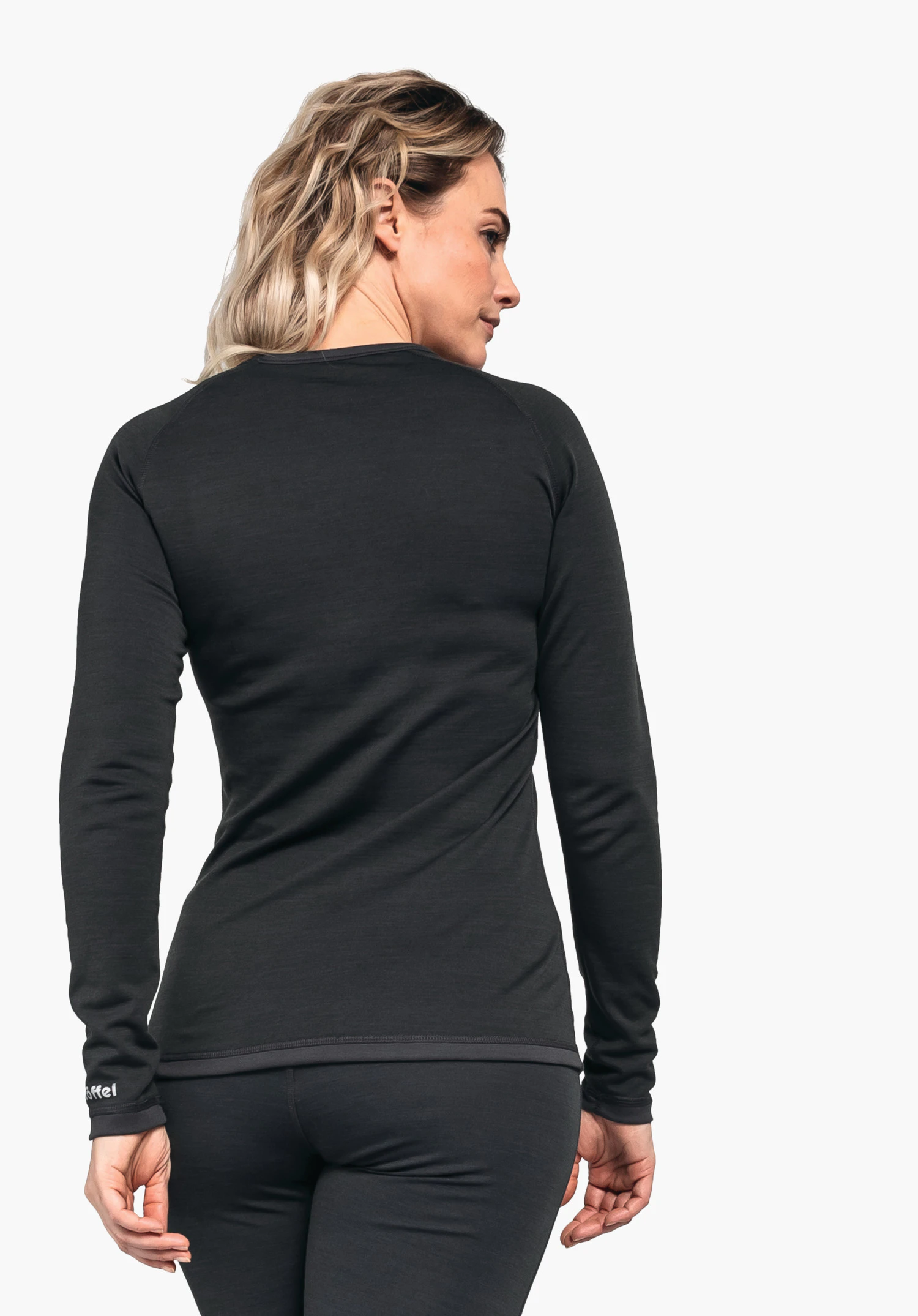 Merino Sport Shirt 1/1 Arm W Langarmshirt (schwarz) trägt eine Frau; steht mit dem Rücken zur Kamera, Kopf seitlich gewendet; neutraler weißer Hintergrund. Text auf Ärmel: "Schöffel"