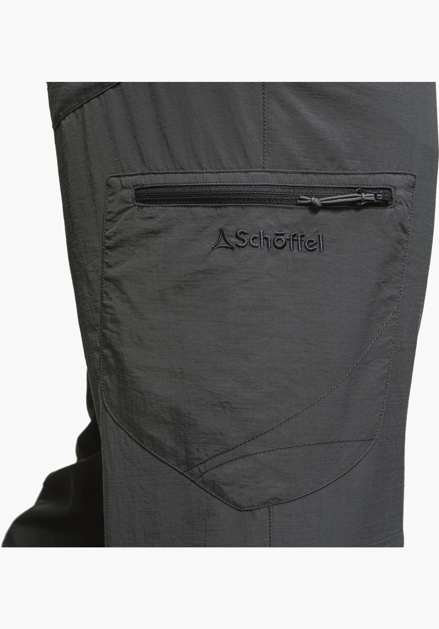 Pants Springdale1 zeigt die aufgesetzte Beintasche in Grau mit einem horizontalen Reißverschluss und dem gestickten Schöffel-Logo. Das funktionale Material und die markanten Design-Nähte betonen den technischen Look für den Outdoor-Einsatz, Nahaufnahme vor weißem/neutralem Hintergrund.