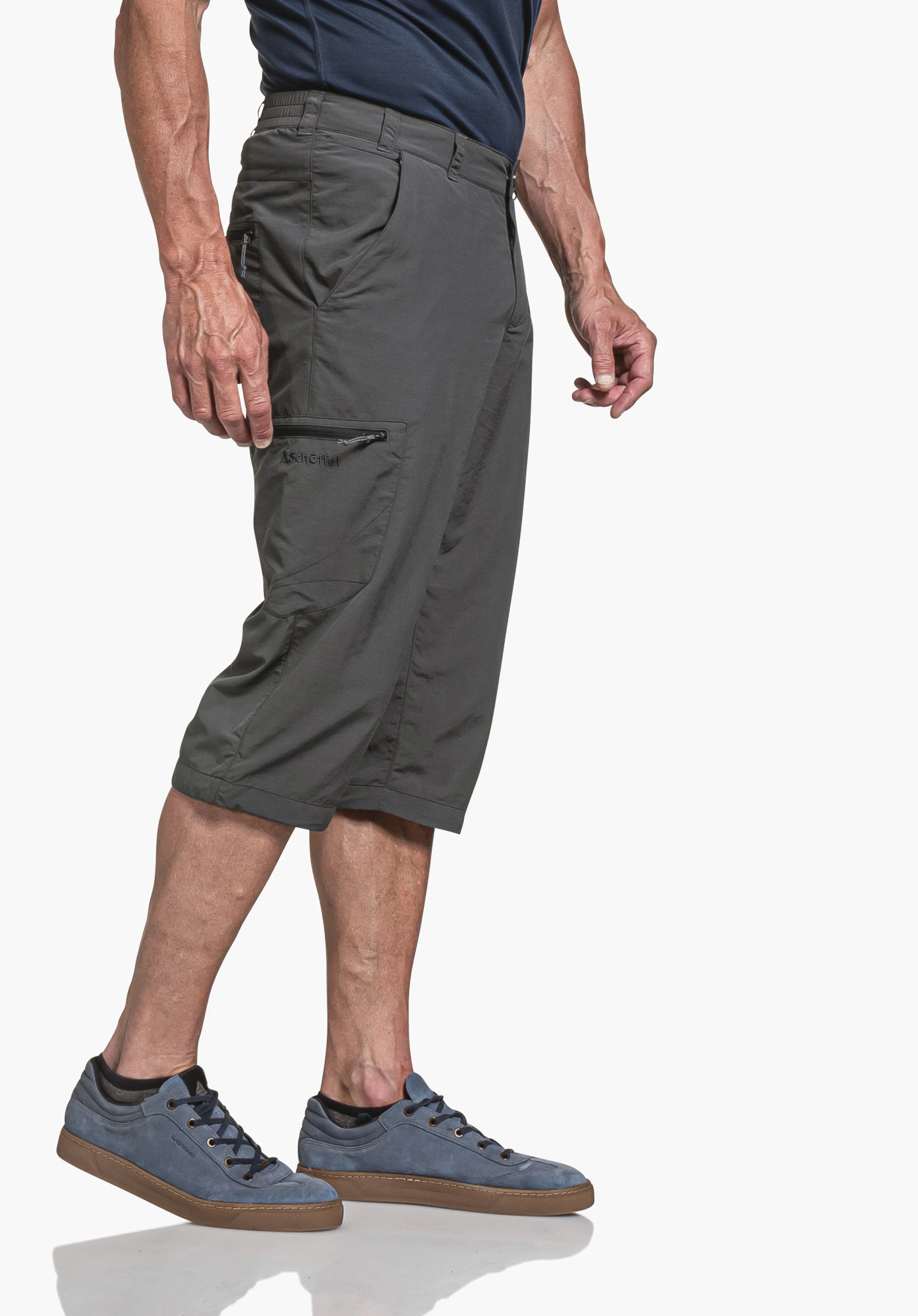 Pants Springdale1 in Grau. Ein Model steht seitlich vor einem neutralen Hintergrund und präsentiert die funktionalen Details der Hose. Das dezente Schöffel-Logo ist gut sichtbar auf der Beintasche platziert.
