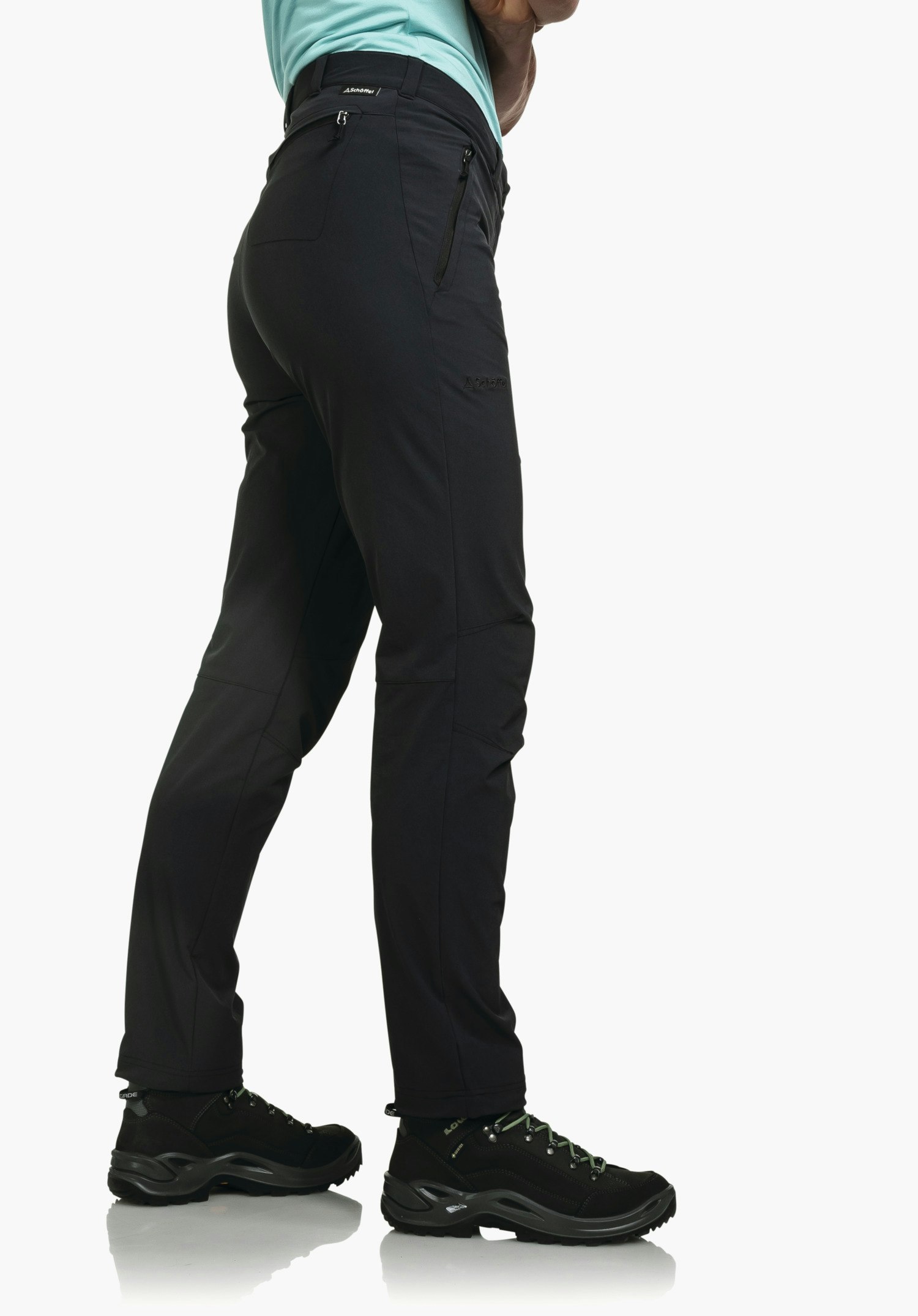Pants Engadin1 deep black outdoor trousers worn by a standing model slightly turned side-on, showing zip pockets and ankle-high hiking boots; white studio background. Text: "Schöffel".
