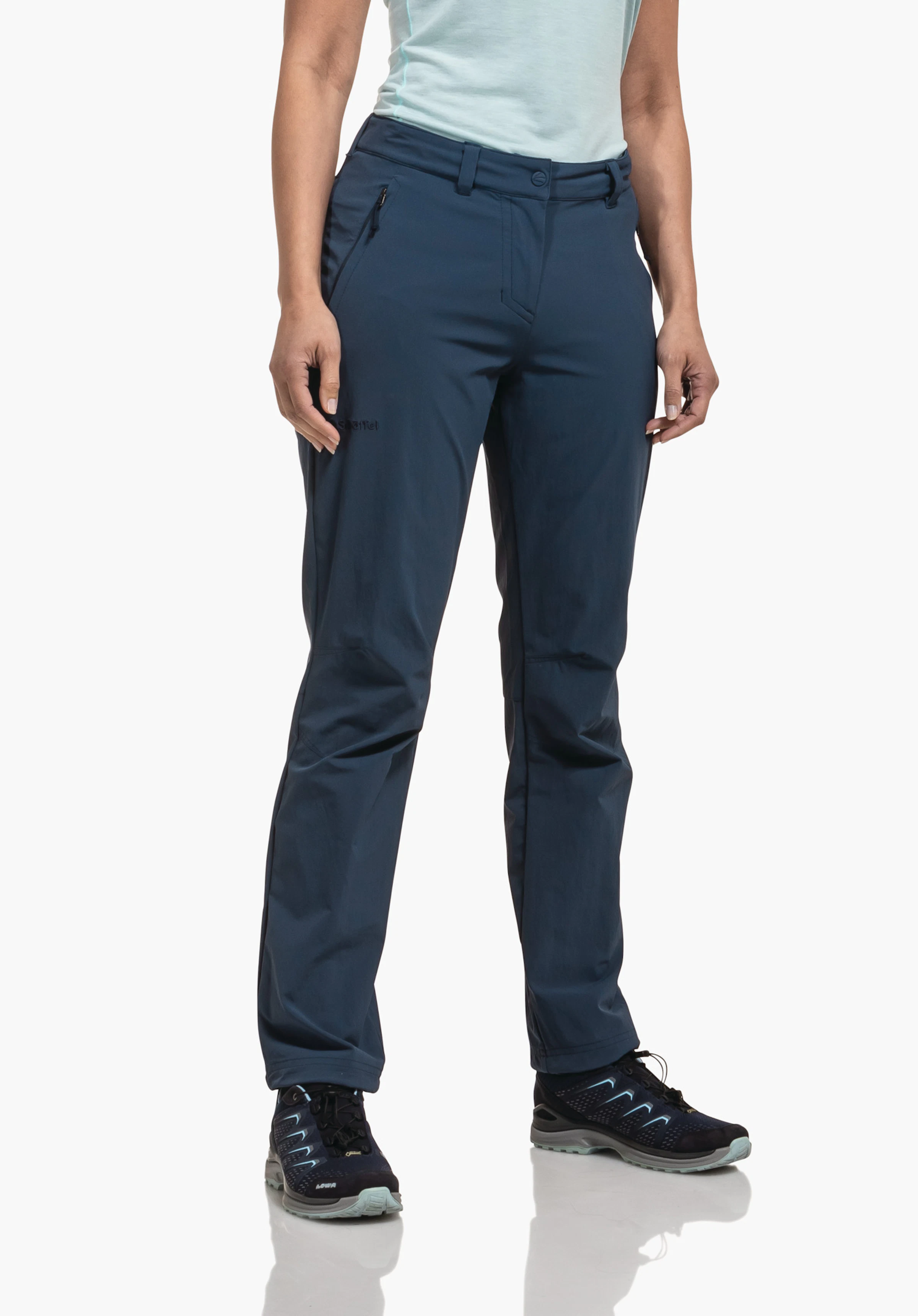 Pants Engadin1 Dunkelblaue Hose, von Frau getragen, steht mit Händen seitlich; hellblaues T-Shirt, dunkle Sportschuhe; weißer Studiohintergrund.