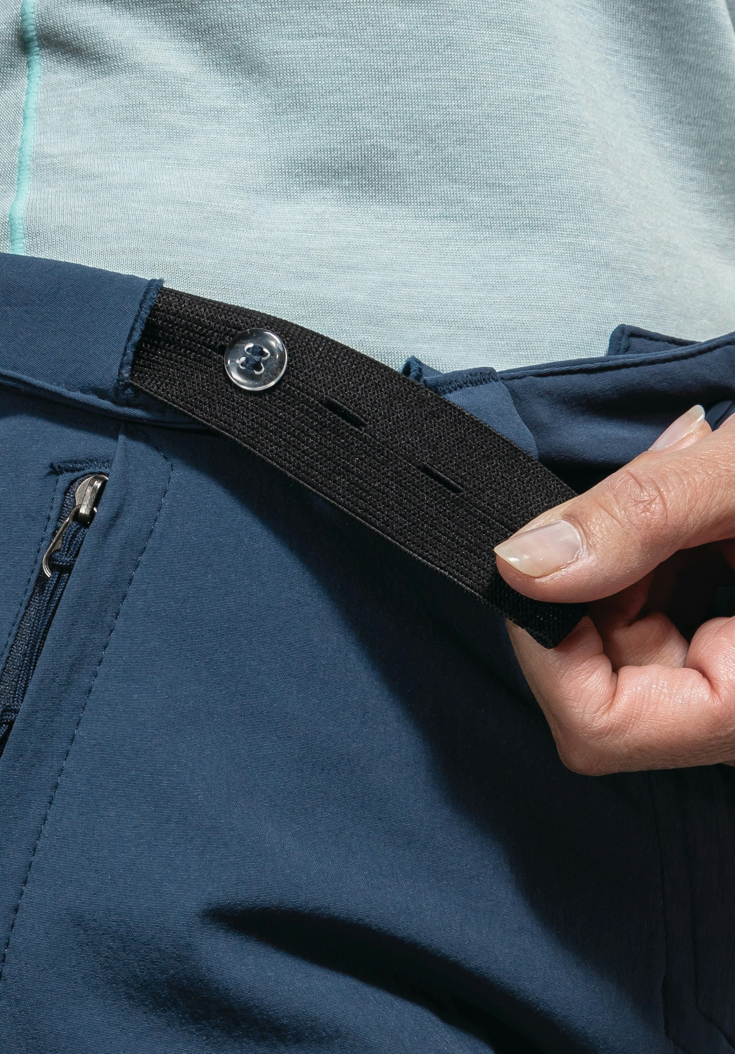 Pants Engadin1 shows the adjustable waistband with black buttonhole elastic and button for an individual fit on the blue material. Close-up against a white/neutral background.