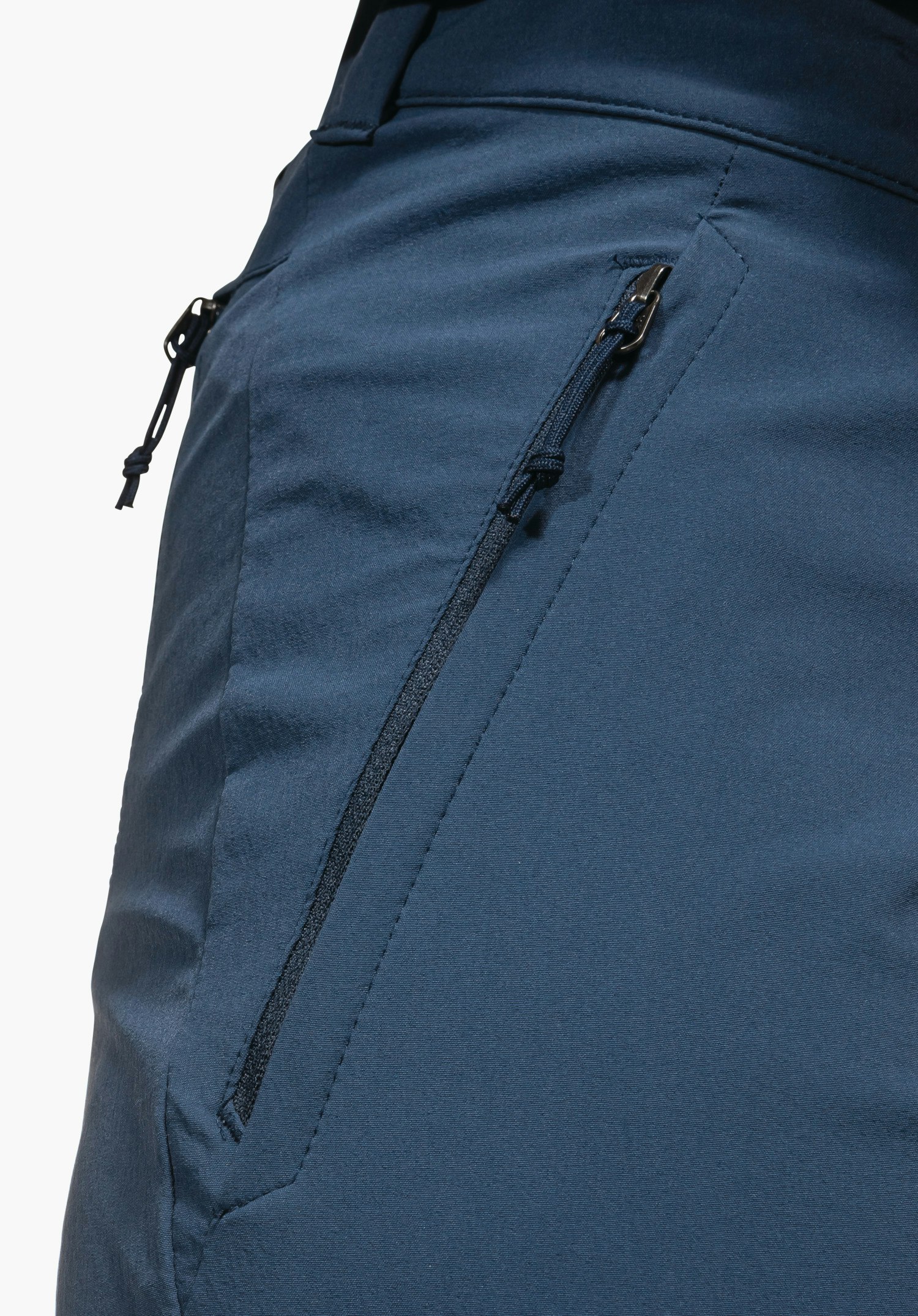 Pants Engadin1 montrant la poche latérale zippée avec cordon sur le tissu bleu, gros plan sur fond blanc/neutre.