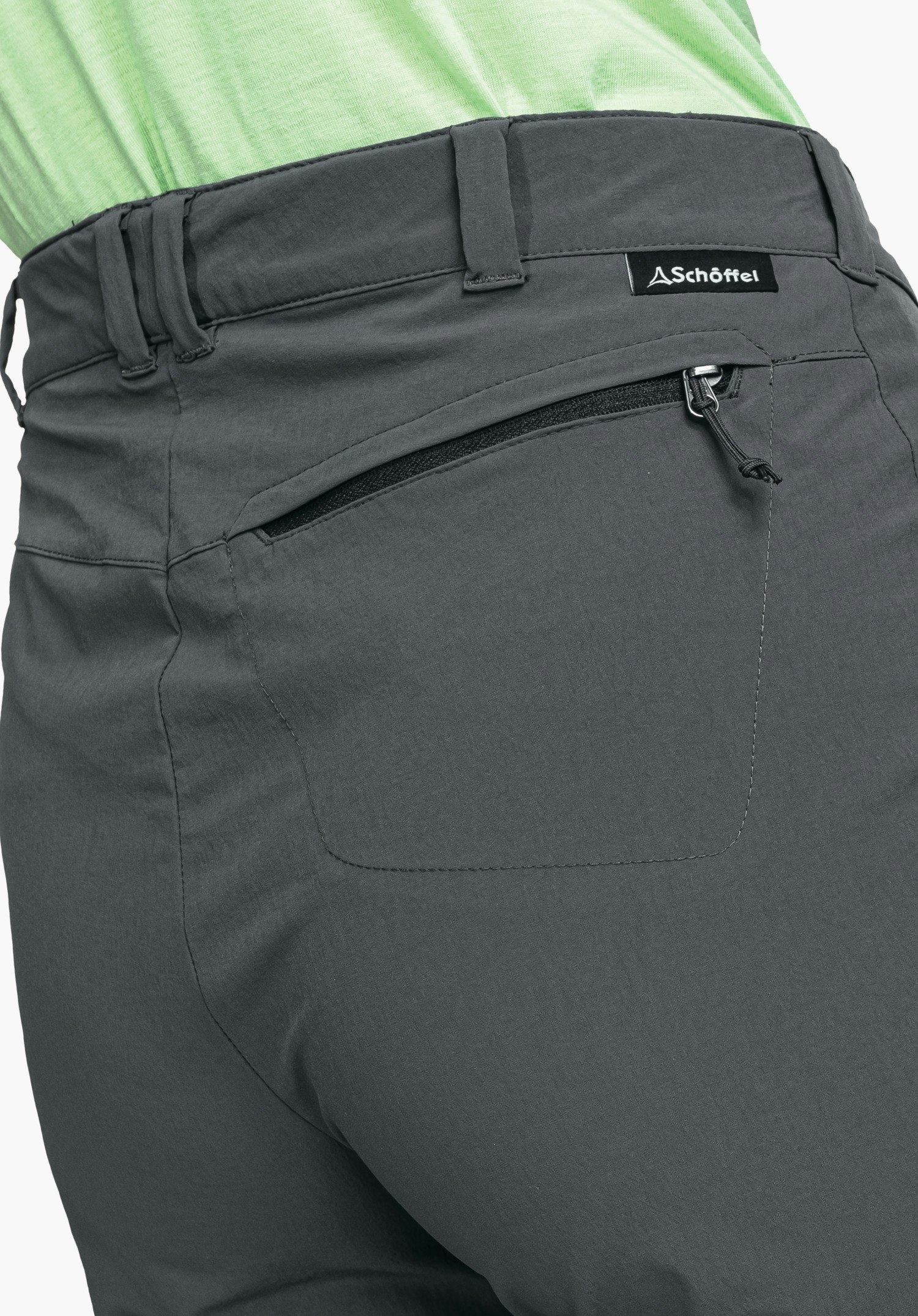 Pants Engadin1 zeigt die graue Gesäßtasche mit Reißverschluss, Gürtelschlaufen und das Schöffel-Logo auf dem Etikett als Nahaufnahme vor weißem Hintergrund.