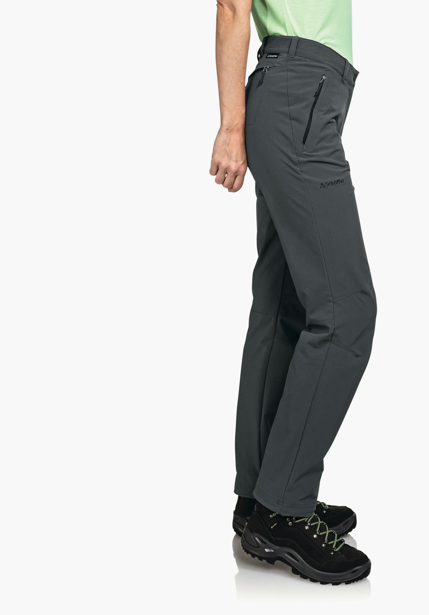 Pants Engadin1 Dunkel grau Wanderhose, seitlich getragen; Person steht entspannt, hell grün Shirt sichtbar; schwarze Wanderschuhe mit grünen Schnürsenkeln; heller, neutraler Hintergrund. Schöffel-Logo. Text: "Schöffel"