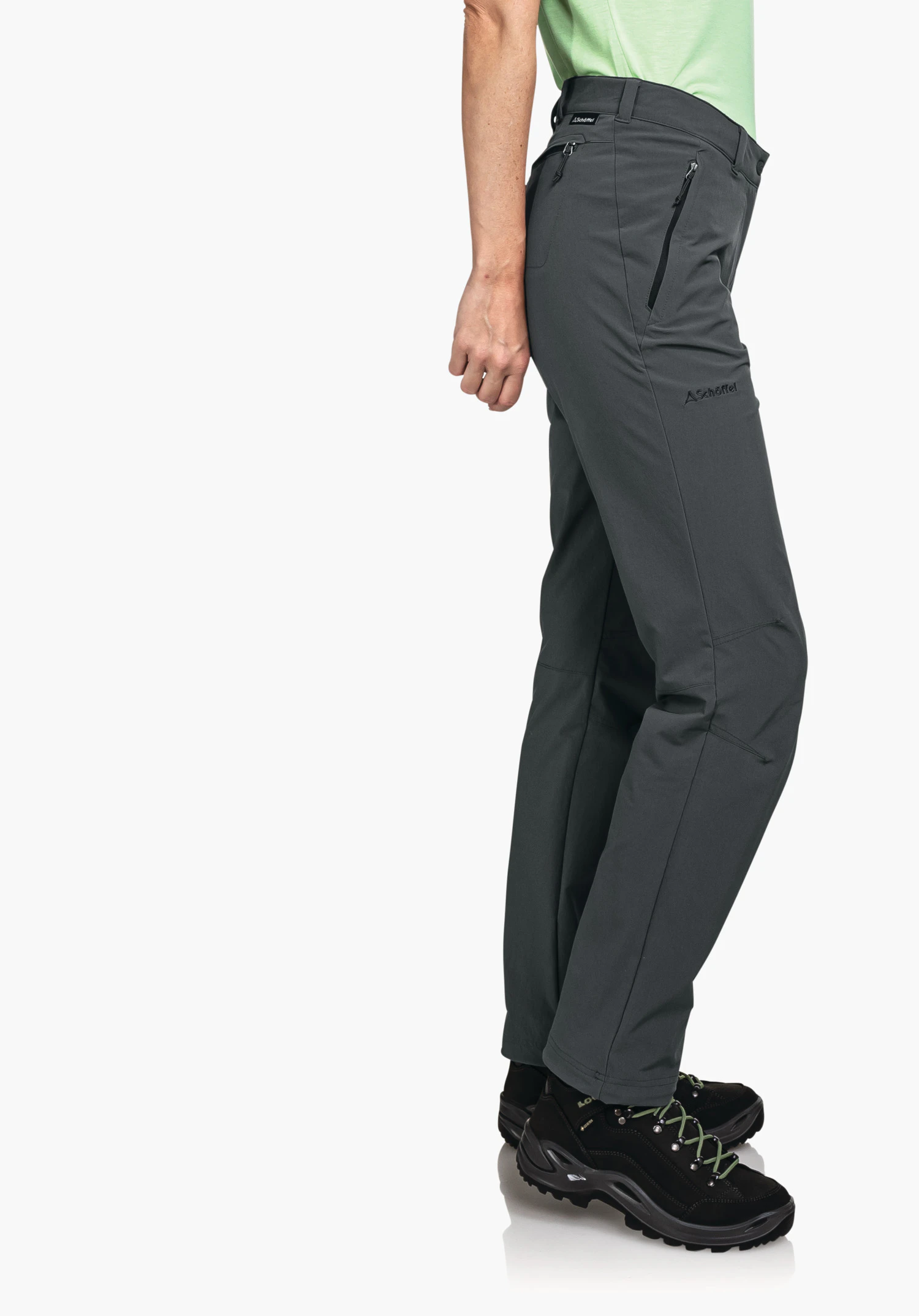 Pants Engadin1 Dunkel grau Wanderhose, seitlich getragen; Person steht entspannt, hell grün Shirt sichtbar; schwarze Wanderschuhe mit grünen Schnürsenkeln; heller, neutraler Hintergrund. Schöffel-Logo. Text: "Schöffel"