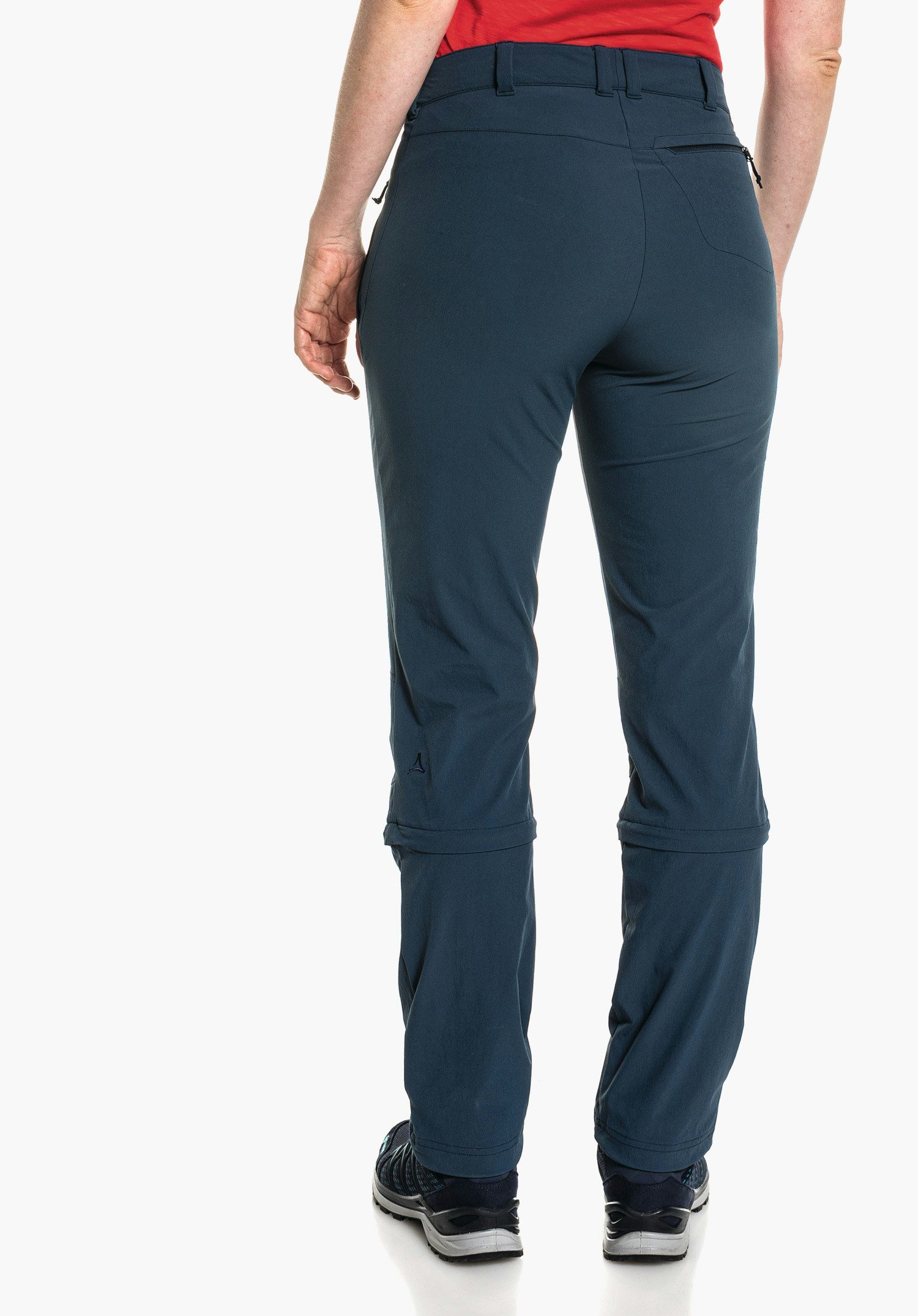 Pants Engadin1 Zip Off dark blue trousers worn from the back; person stands against a white background, red top, black shoes; knee seam visible, Schöffel logo on the left calf.