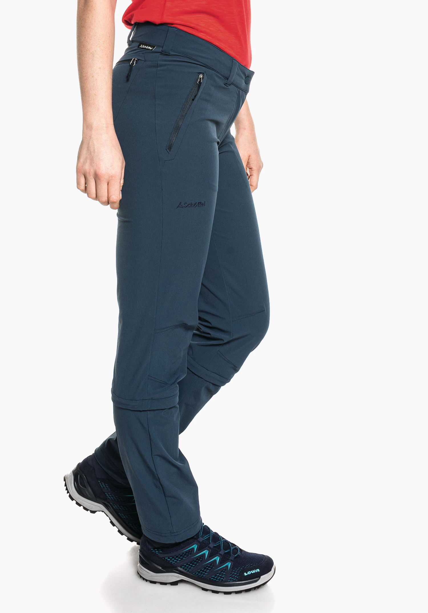 Pants Engadin1 Zip Off pantalon de randonnée bleu foncé porté de profil par une personne debout devant fond blanc; logo Schöffel et inscription 'Schöffel' visibles sur la cuisse; chaussure avec inscription 'LOWA'.