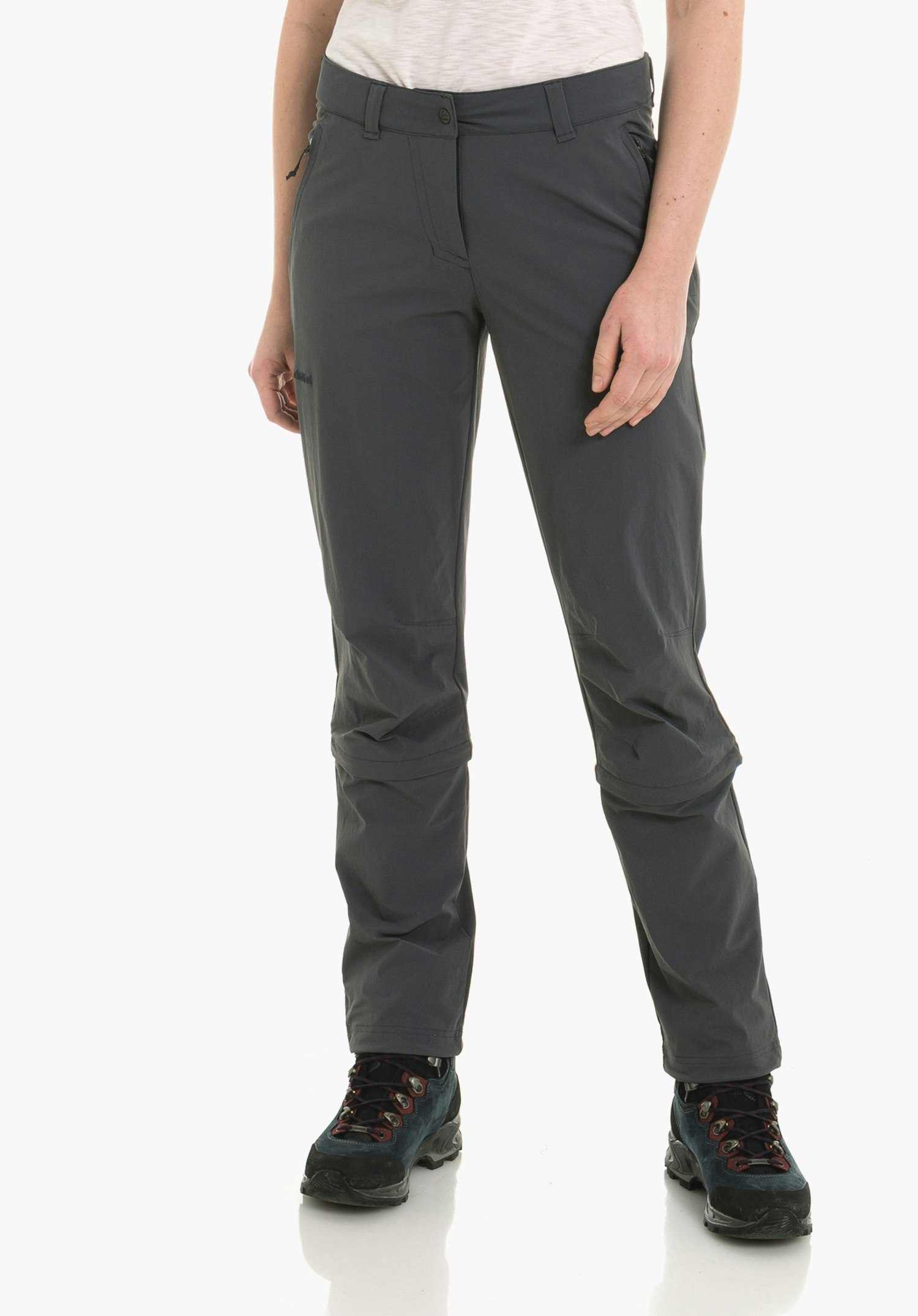 Pants Engadin1 Zip Off dunkelgraue Wandershose, getragen von stehender Person mit weißem Shirt und dunkelblauen Wanderschuhen; Text auf Hose: "Schöffel". Vor weißem Hintergrund.
