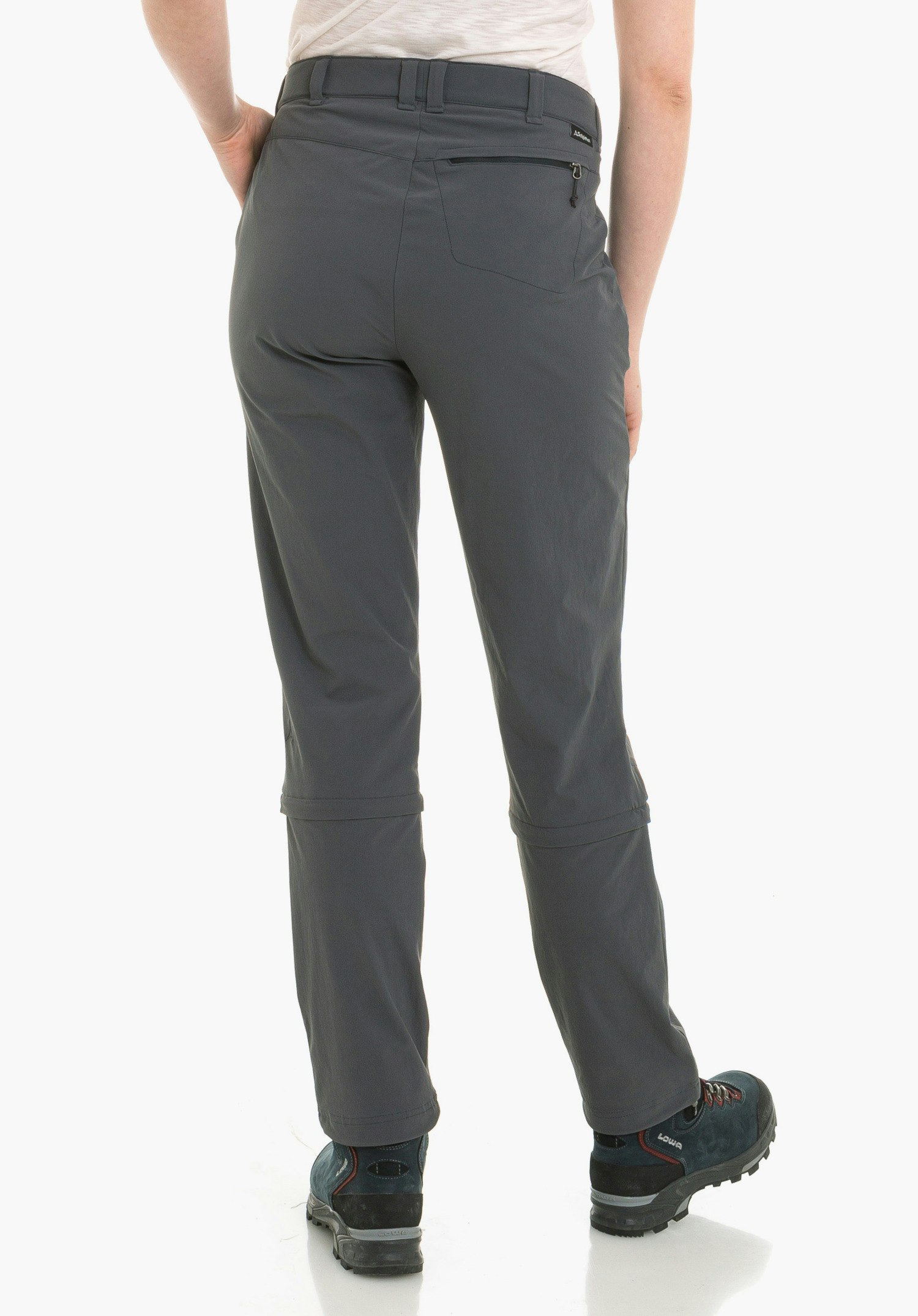Pants Engadin1 Zip Off dark grey zip-off trousers worn from the back; person stands wearing dark blue hiking boots with “LOWA” lettering; white studio background.