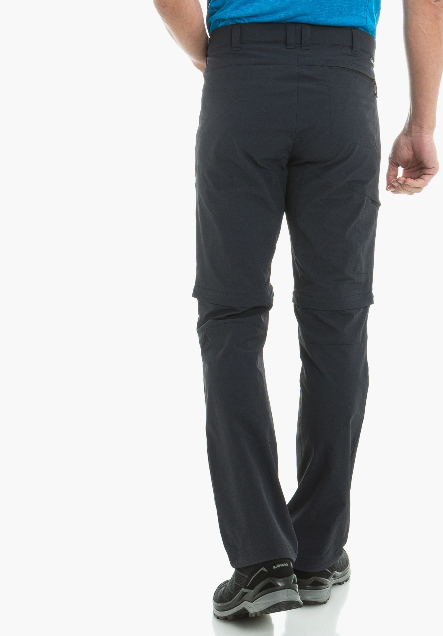 Pants Koper1 Zip Off dark blue hiking trousers seen from the back; person walking on a white background, wearing a light blue top and black hiking shoes; “LOWA” text on the heel.