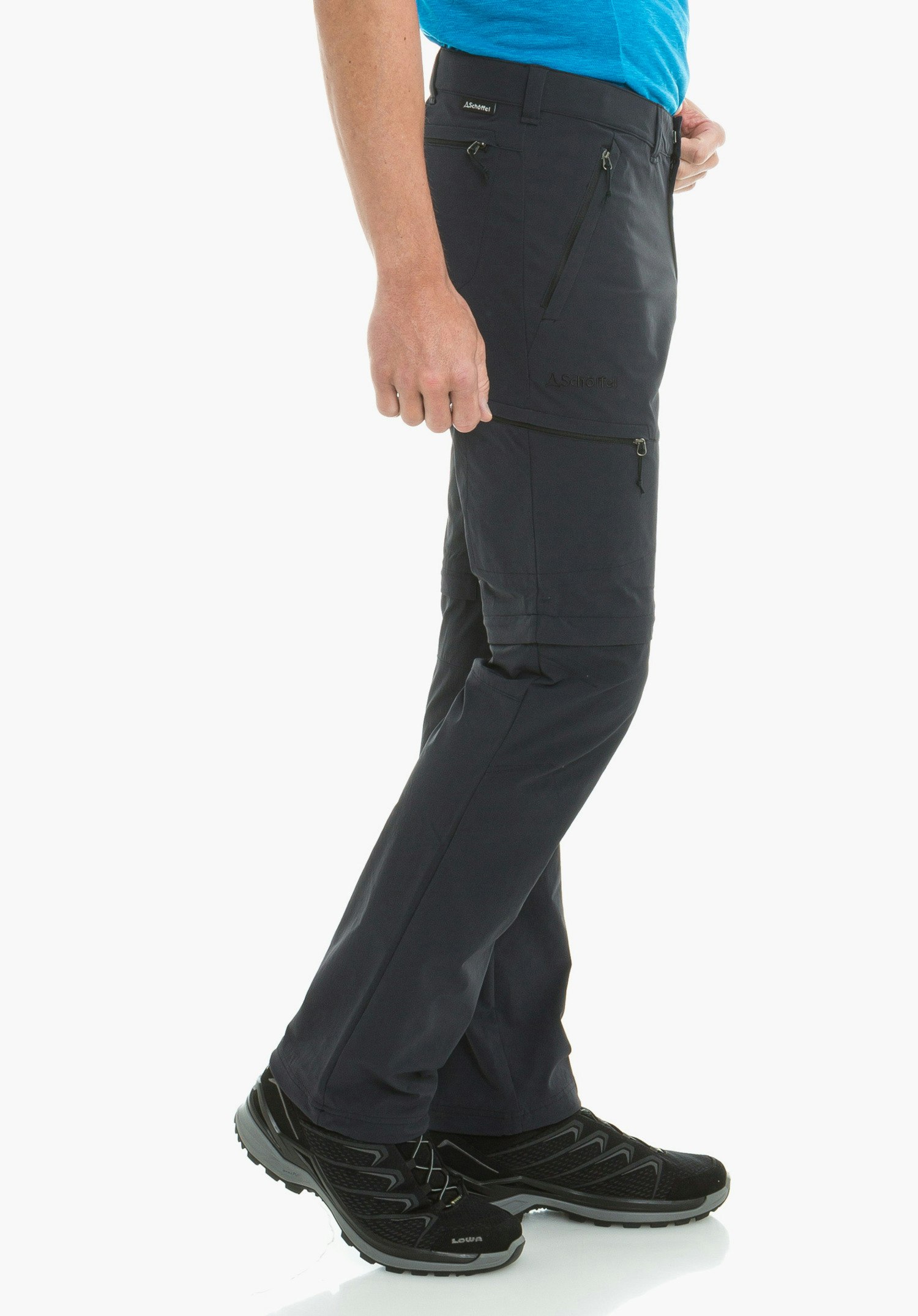 Pants Koper1 Zip Off dunkelblaue Wanderhose, Person steht seitlich und hält den Hosenbund, Reißverschlusstaschen sichtbar, hellblaues Shirt, schwarze Wanderschuhe; Text: "A.Schöffel", "Schöffel", "LOWA".