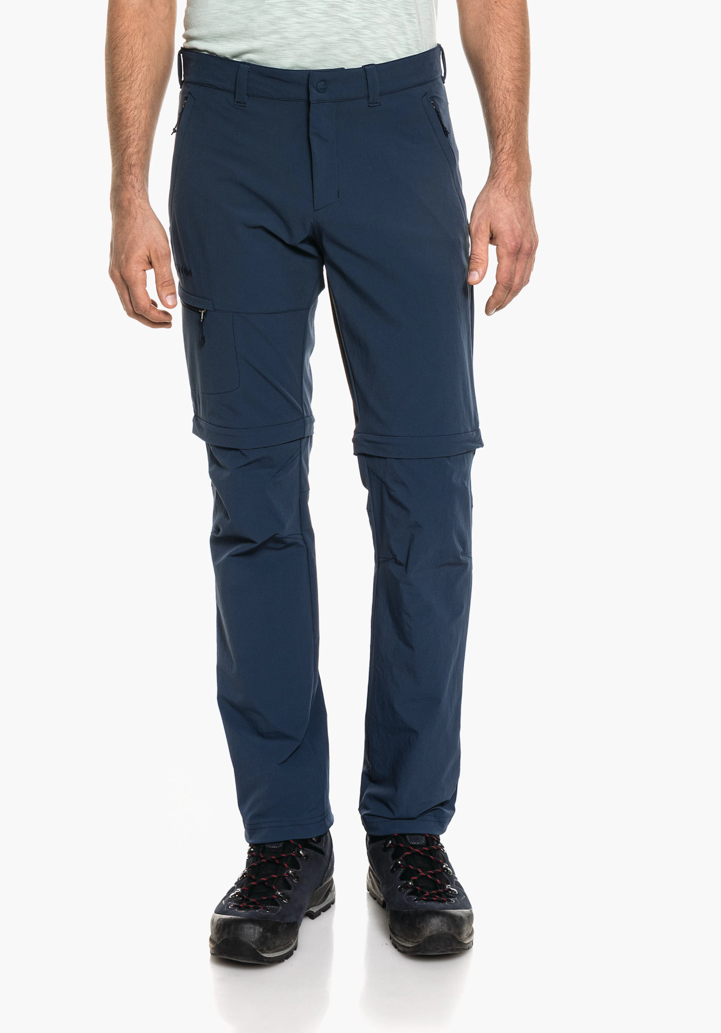 Pants Koper1 Zip Off Dunkelblaue zip-off Wanderhose, getragen, Hosenbeine abnehmbar, Schöffel-Logo am linken Oberschenkel; kombiniert mit schwarzen Wanderstiefeln, auf weißem Hintergrund.