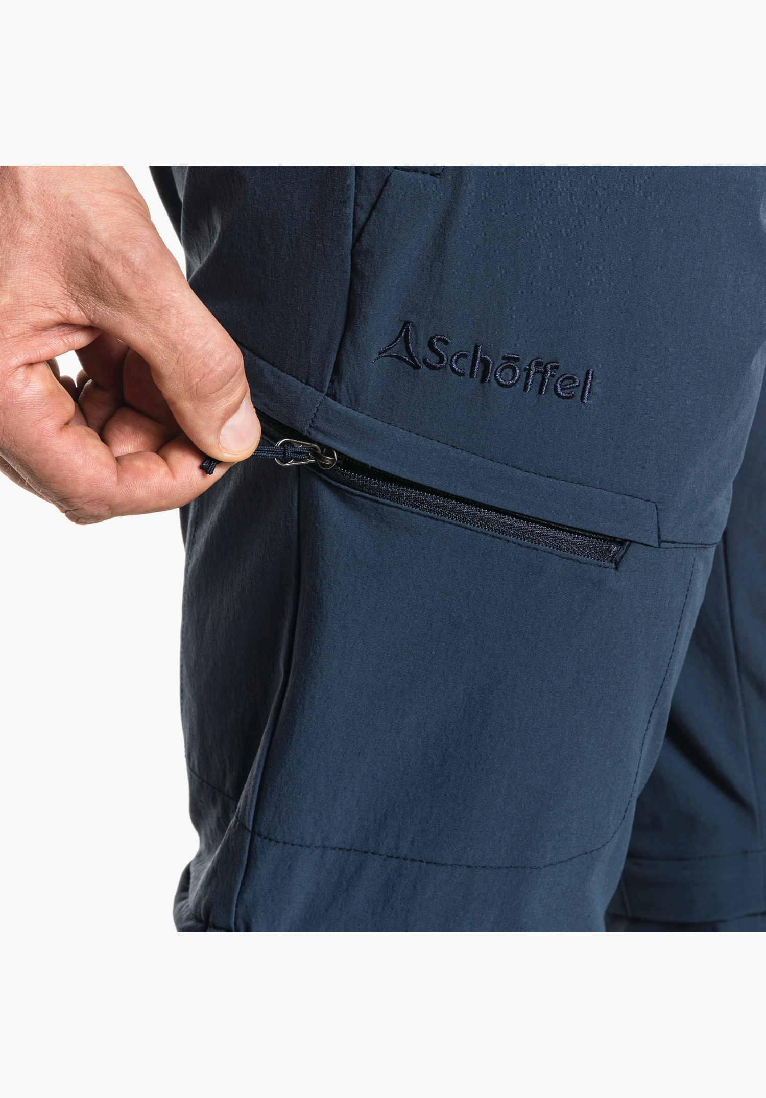 Pants Koper1 Zip Off features the zip of the thigh pocket on the blue fabric alongside the embroidered Schöffel logo. Close-up against a white/neutral background.