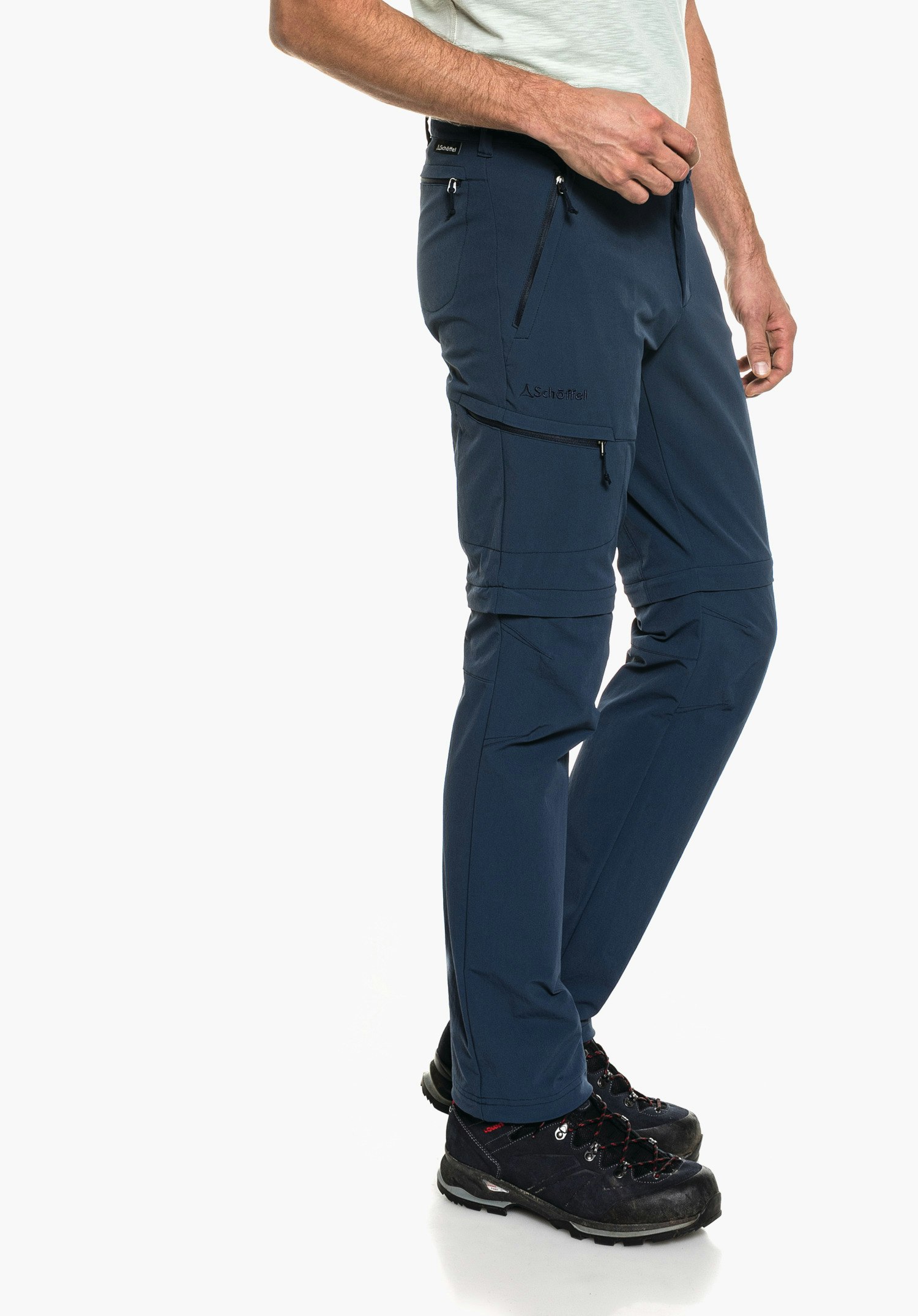 Pants Koper1 Zip Off Dunkel blau Zip-off Wanderhose, getragen von stehender Person, Reißverschlüsse an Oberschenkel und Hüfte, schwarz Wanderschuhe, weißer Hintergrund; Beschriftung: "Schöffel", Schöffel-Logo.