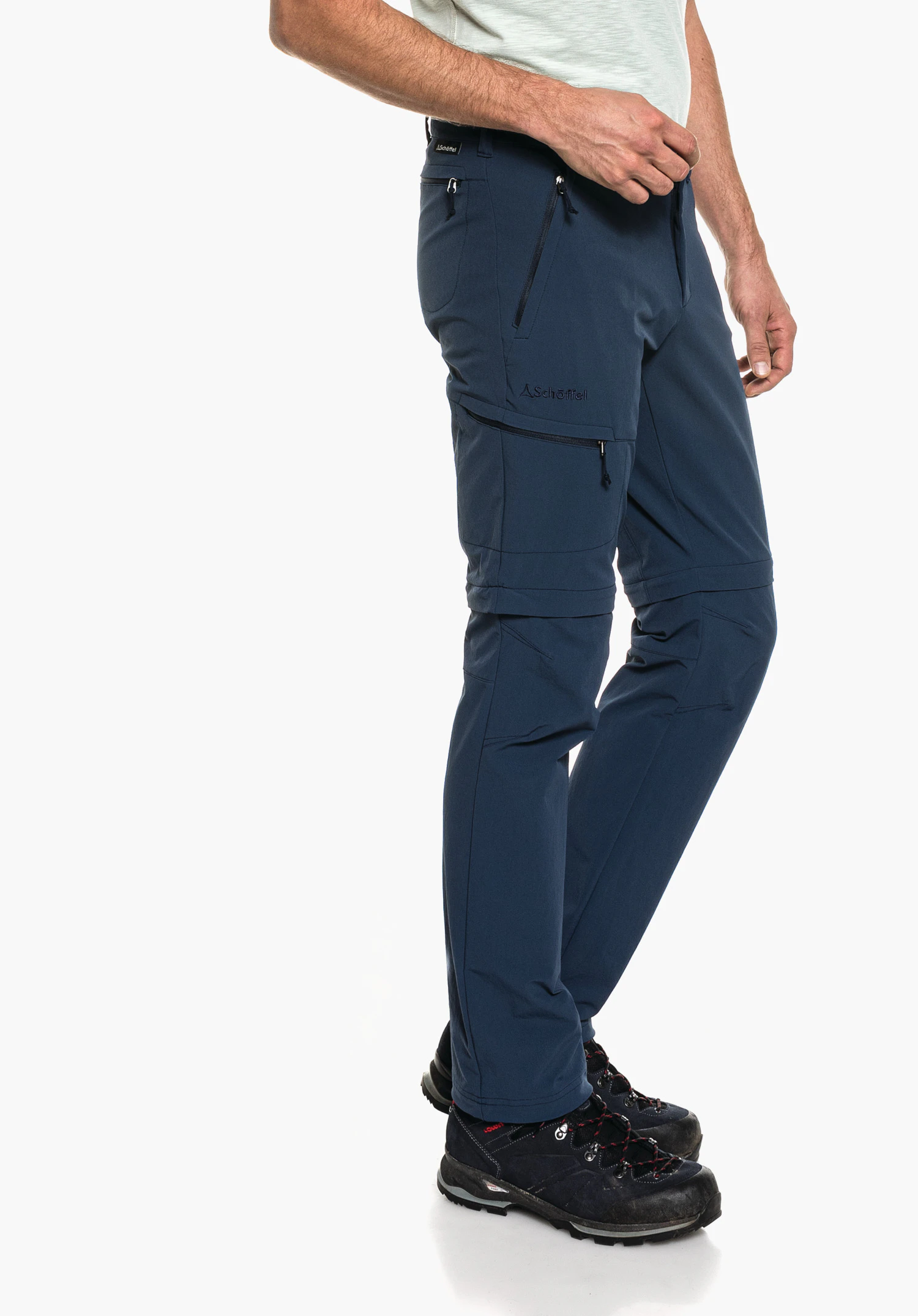 Pants Koper1 Zip Off dark blue zip-off hiking trousers worn by a standing person, zips on thigh and hip visible, black hiking boots, white background; labelling: "Schöffel", Schöffel logo.