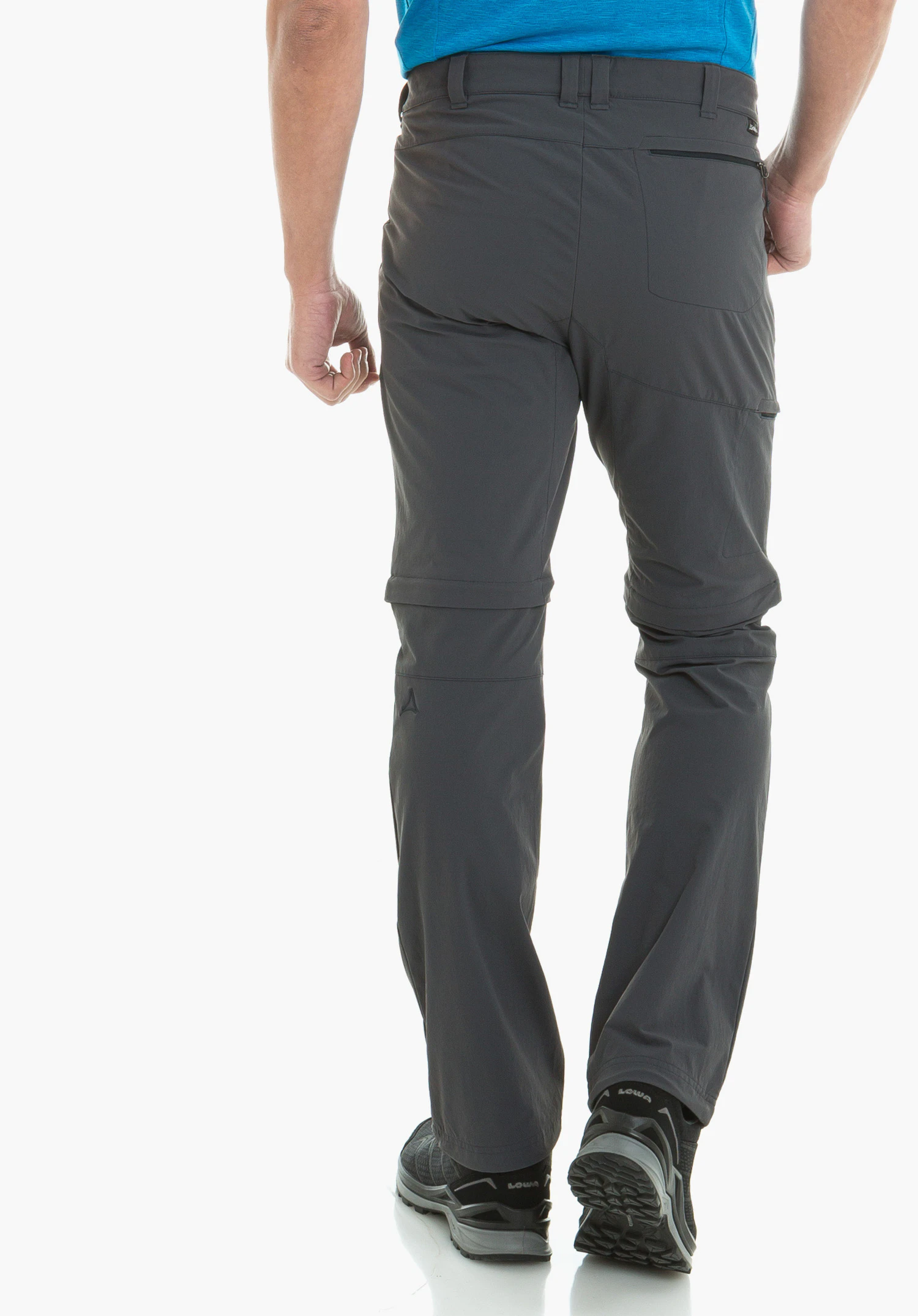 Pants Koper1 Zip Off dark grey zip-off trousers with Schöffel logo, worn by a person walking away; light blue shirt and black hiking shoes with “LOWA” text; white background.