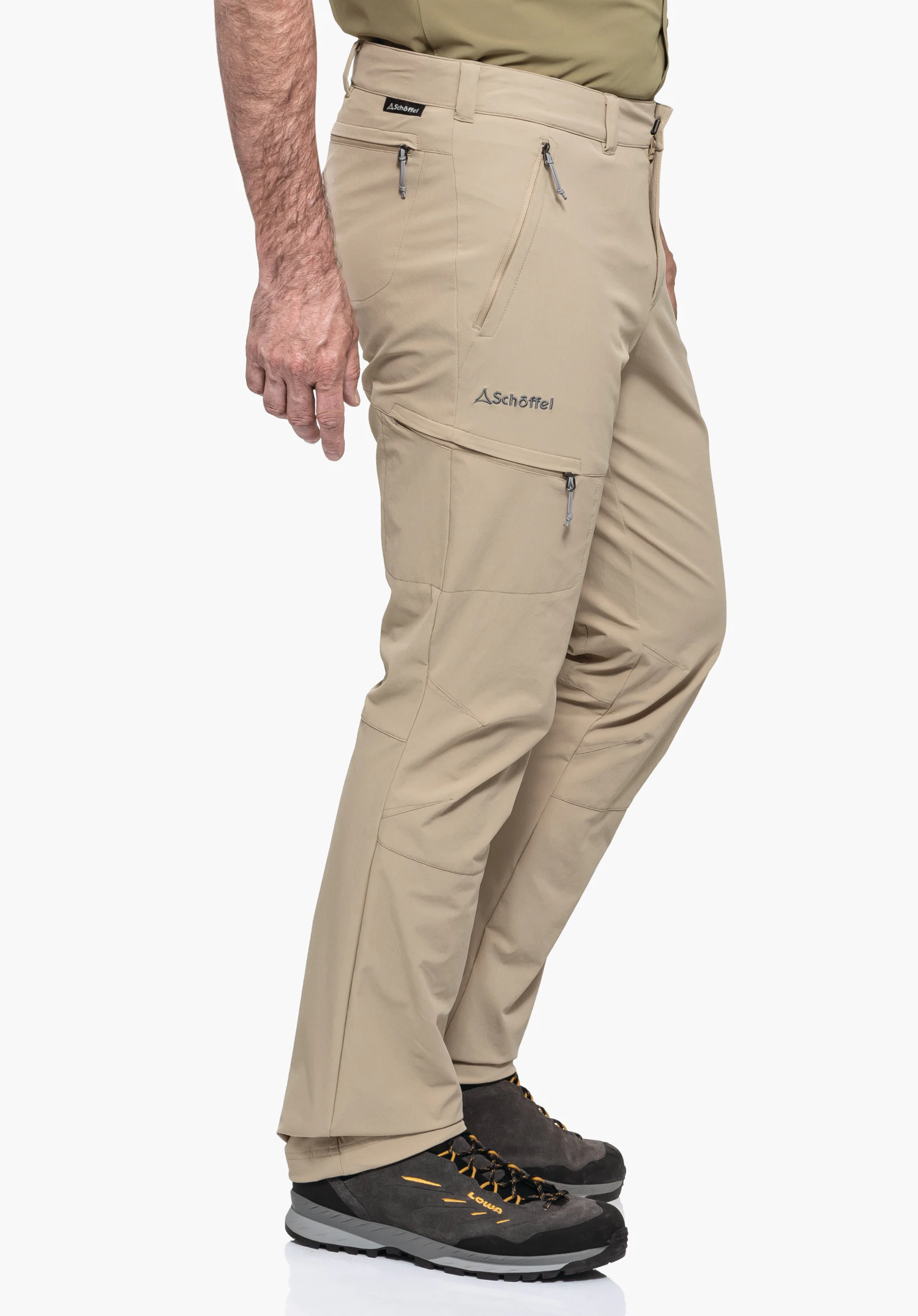 Pants Koper1 on a model standing sideways. The trousers in beige feature practical zip pockets and the Schöffel logo on the thigh, presented against a neutral background.