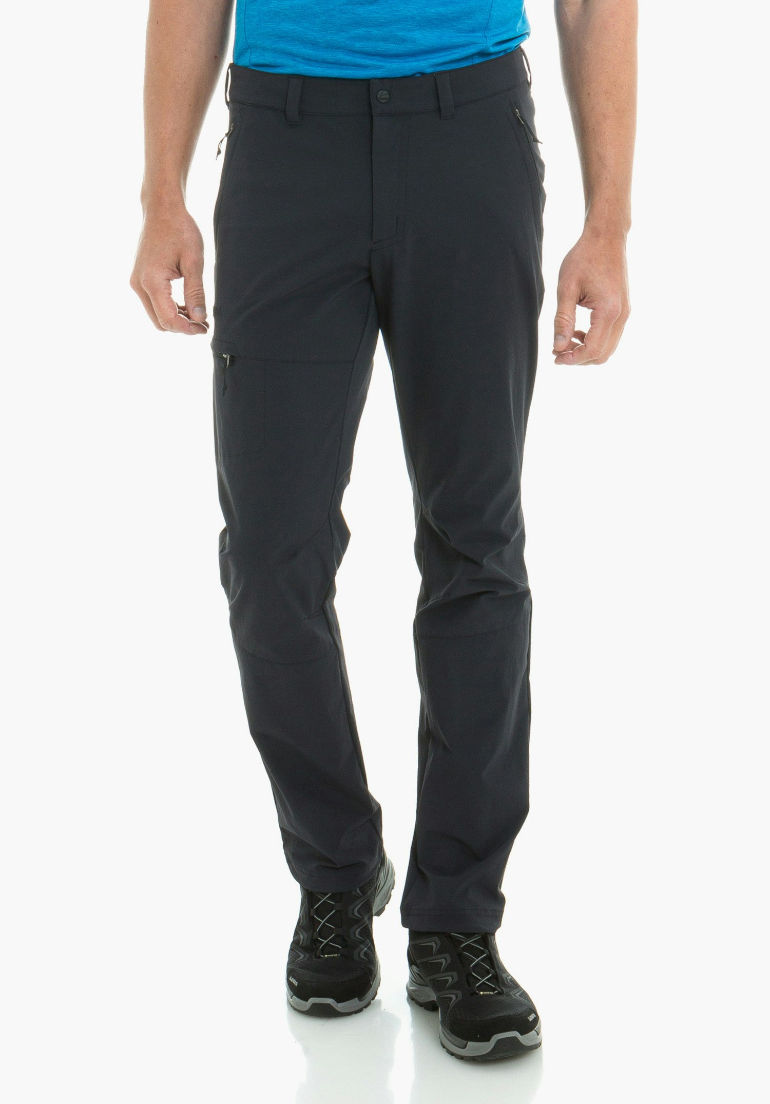 Pants Koper1 Pantalon bleu foncé porté par un homme debout; jambes légèrement écartées, mains le long du corps; chaussures de randonnée noires, bord d’un t-shirt bleu clair visible; fond blanc lumineux.