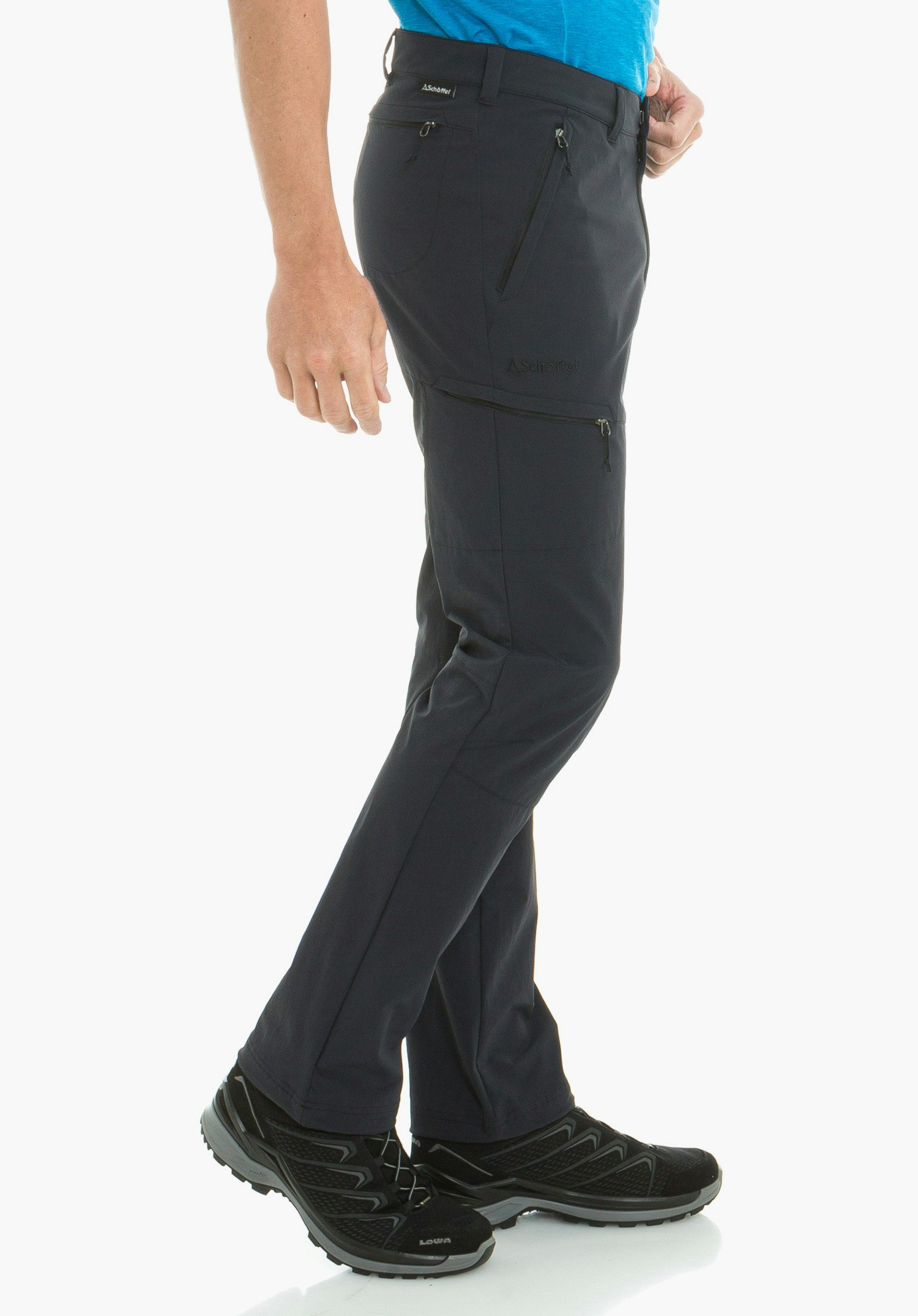 Pants Koper1 pantalon bleu foncé, porté de profil par une personne debout avec poches zippées; t-shirt bleu clair et chaussures noires; fond blanc. Textes: "Schöffel", "LOWA".