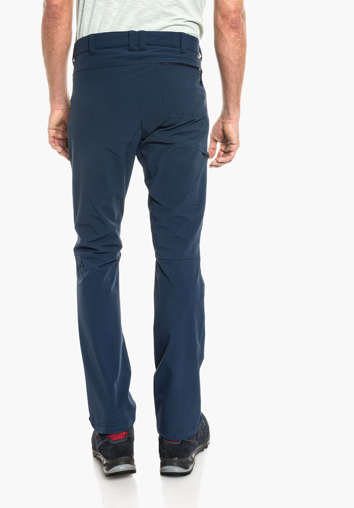 Pants Koper1 dark blue trousers worn from the back by a standing person; rear zip pocket, Schöffel logo at the waistband, light green shirt hem visible, dark blue shoes with red heel accent.