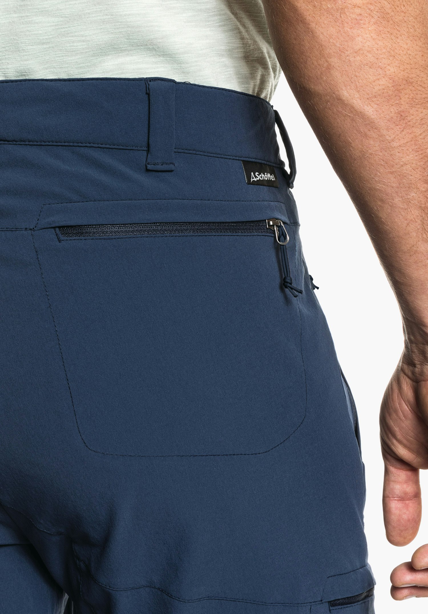 Pants Koper1 montre la poche arrière zippée bleue, les passants de ceinture et la petite étiquette logo Schöffel en gros plan sur fond blanc/neutre.