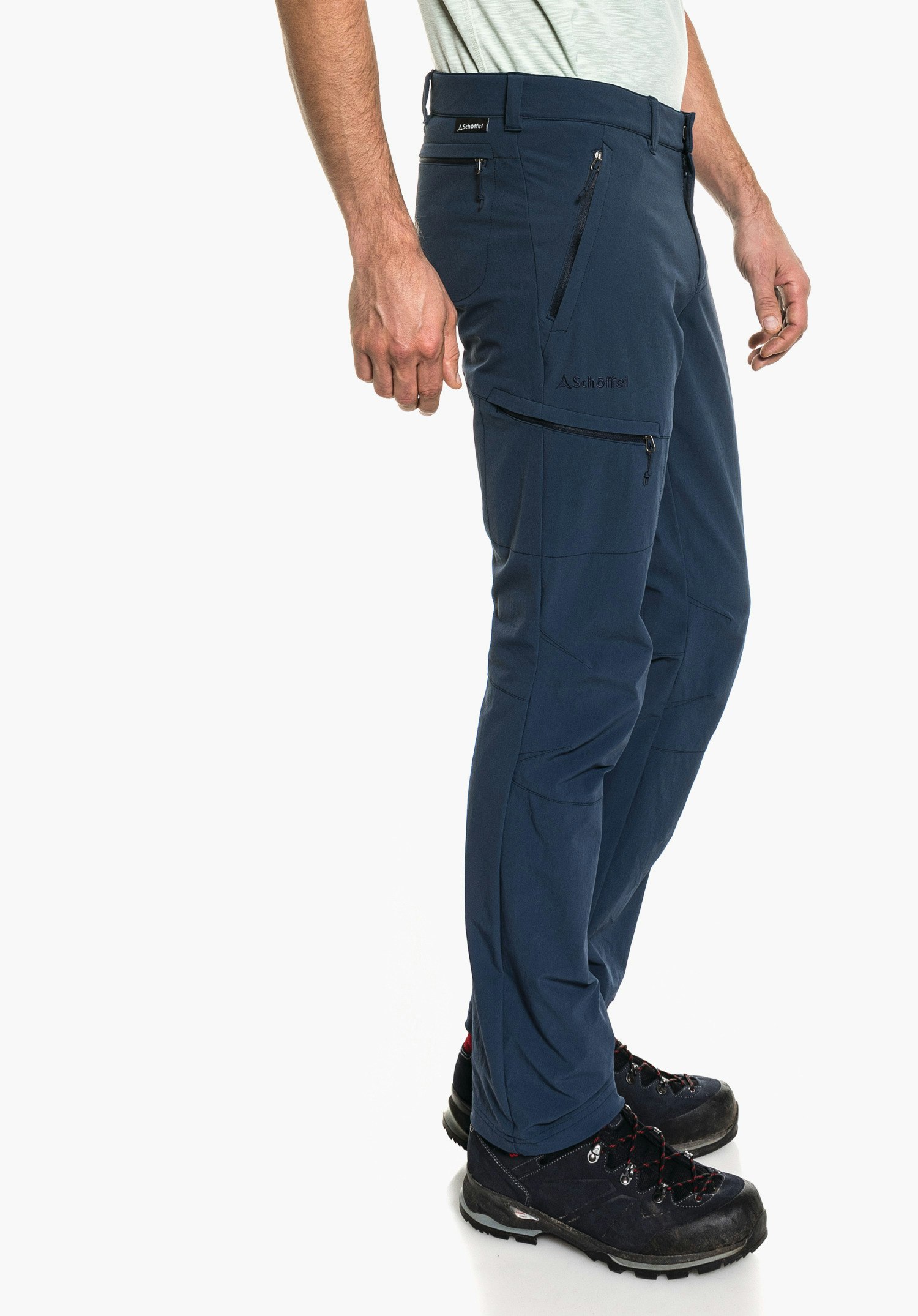 Pants Koper1 pantalon outdoor bleu foncé porté par une personne debout, légèrement de profil et immobile, avec plusieurs poches zippées et chaussures de montagne noires; fond blanc. Texte: "Schöffel".