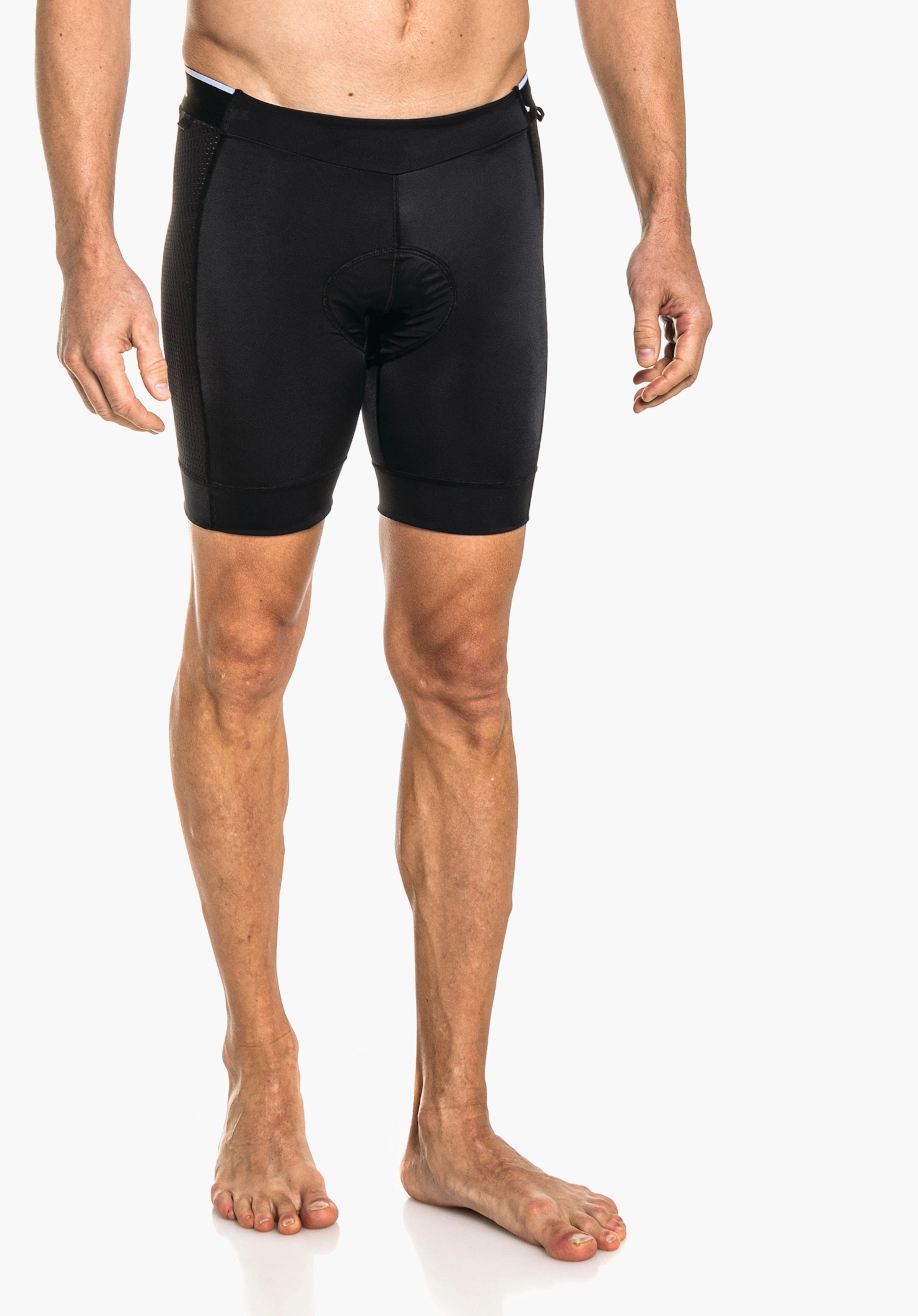 Skin Pants 4h M black cycling shorts worn on the male pelvis with padding visible at the front; man stands barefoot; short tight legs; white studio background.