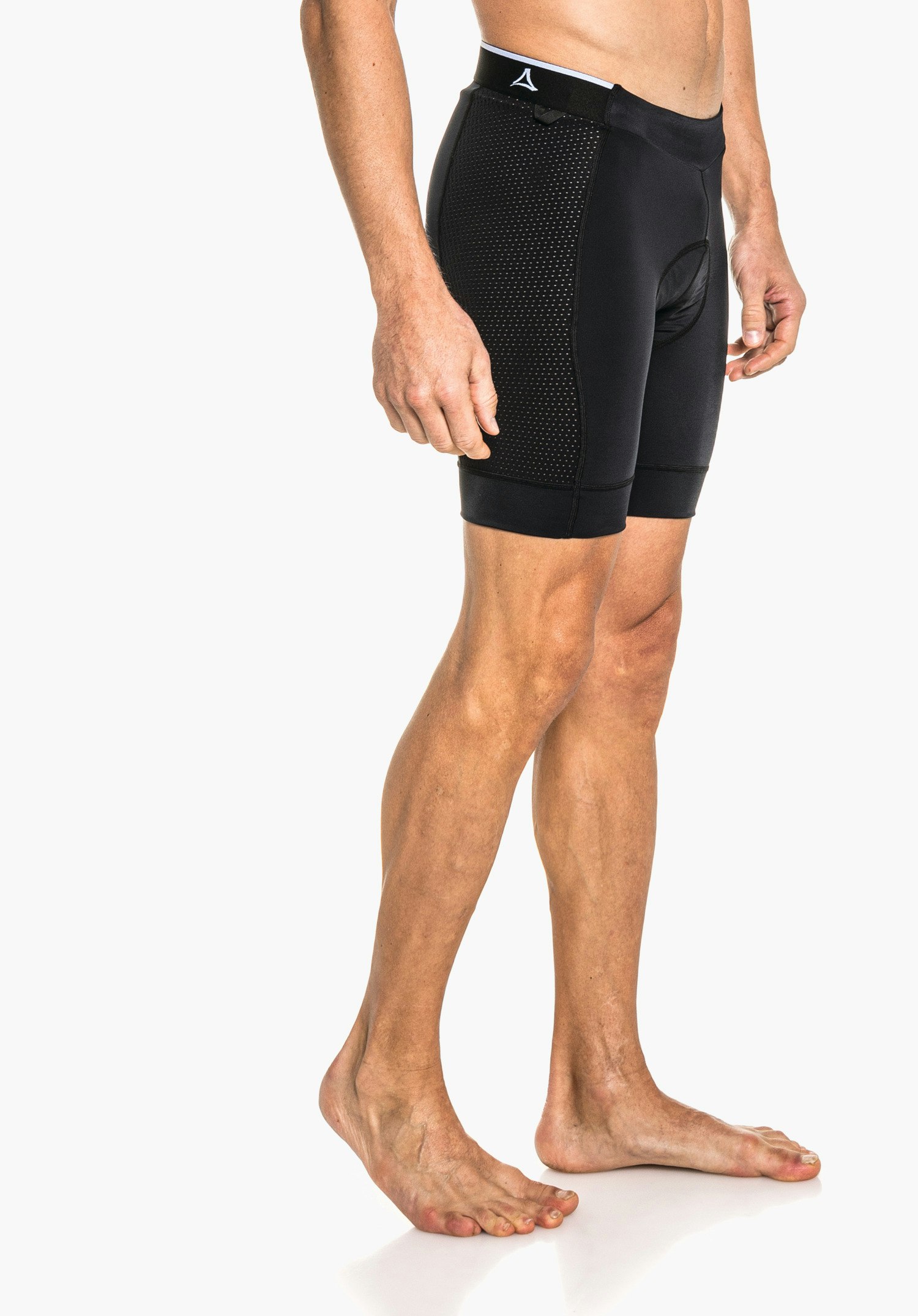 Skin Pants 4h M Schwarze Rad-Shorts mit Schöffel-Logo am Taillenbund, eng sitzend an nackten männlichen Beinen; Person steht barfuß vor weißem Hintergrund.