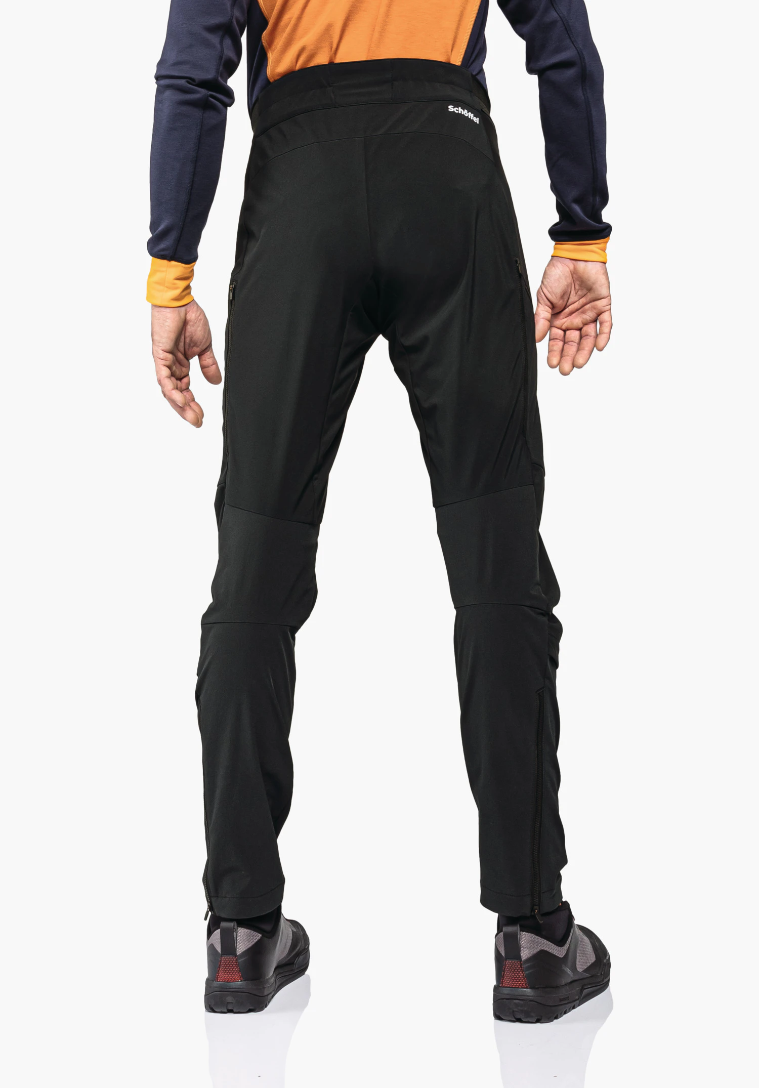 Skin Pants Warm 4h M zwarte leggings, strak rond zitvlak en benen; persoon trekt het shirt omhoog, achteraanzicht voor lichte achtergrond, blootsvoets. Schöffel-logo; opschrift: "Schöffel".