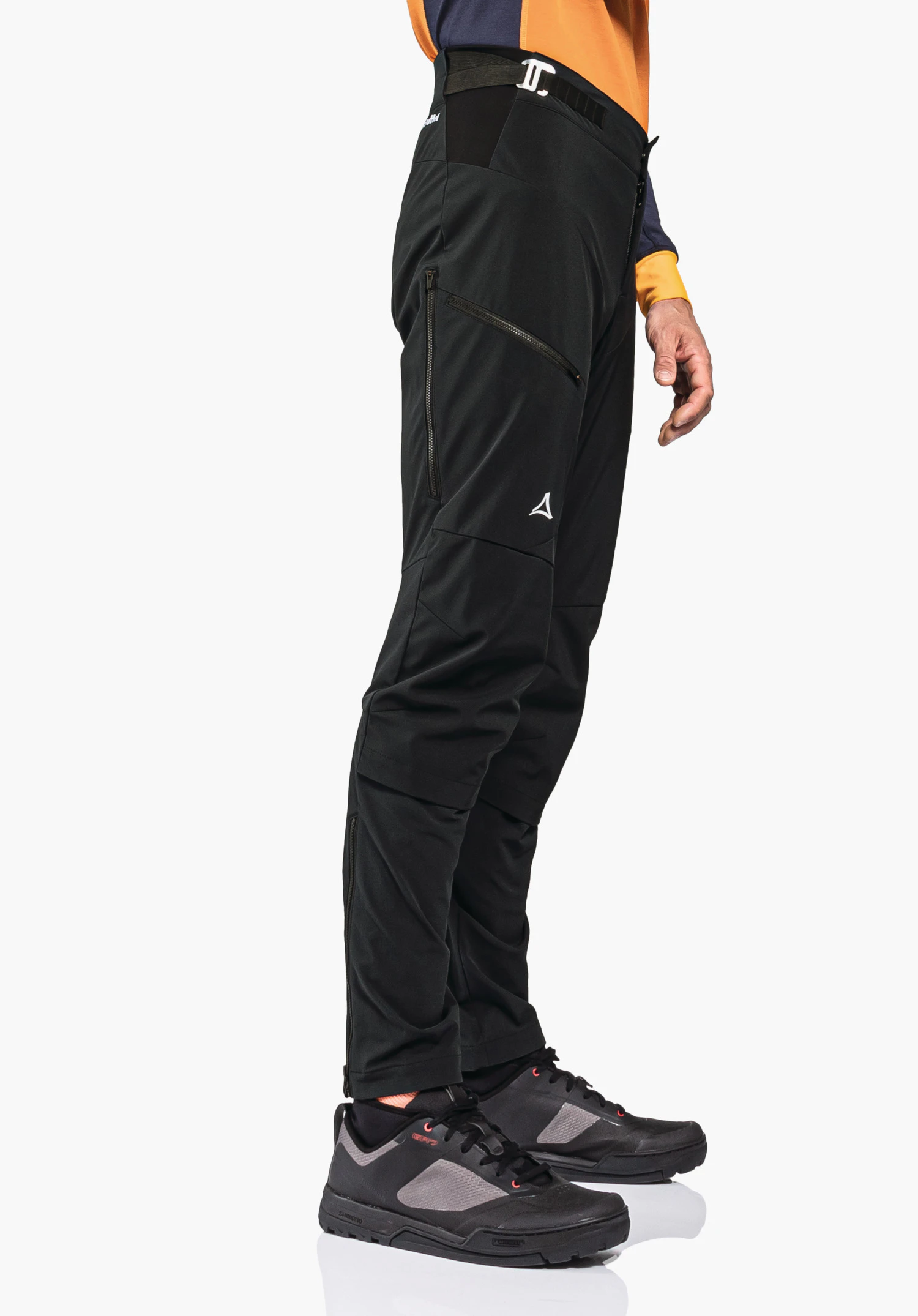 Hybrid Pants Tree Run M zwarte outdoorbroek met Schöffel-logo, zijwaarts gedragen door een staande persoon; oranje/donkerblauw bovenstuk, donkergrijze/lichtgrijze schoenen, witte achtergrond. Tekst: Schöffel.