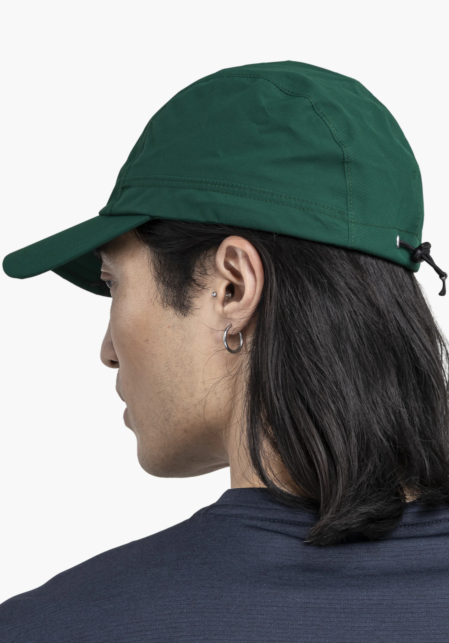 Rain Cap3. Het model staat zijwaarts in profiel en draagt de groene pet, waardoor het verstelbare trekkoord aan de achterkant duidelijk zichtbaar is, gefotografeerd tegen een neutrale achtergrond.