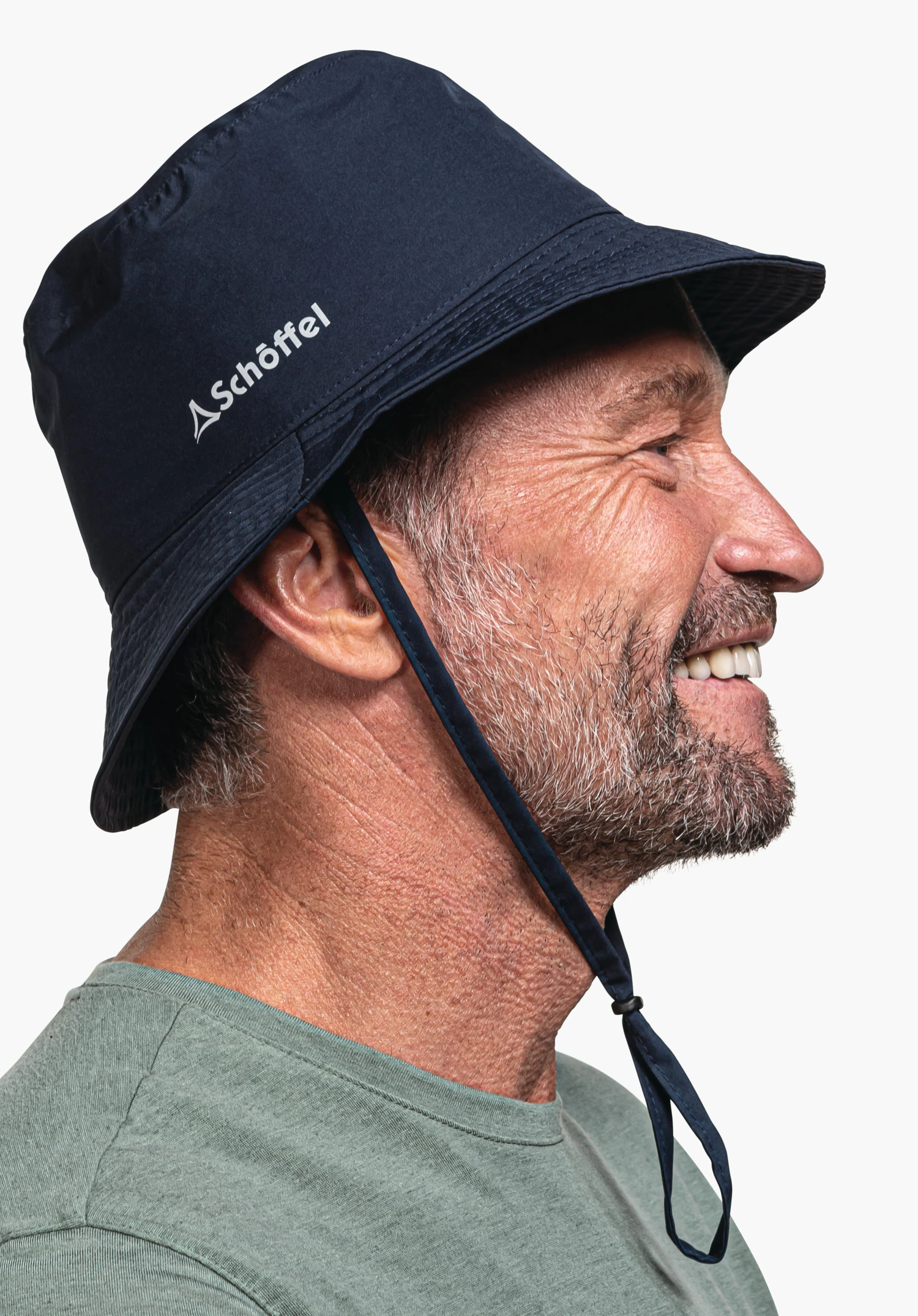 Rain Hat4 in Blau: Ein lächelndes Model steht seitlich vor einem neutralen Hintergrund und trägt den Hut, bei dem das weiße Schöffel-Logo deutlich an der Seite erkennbar ist.