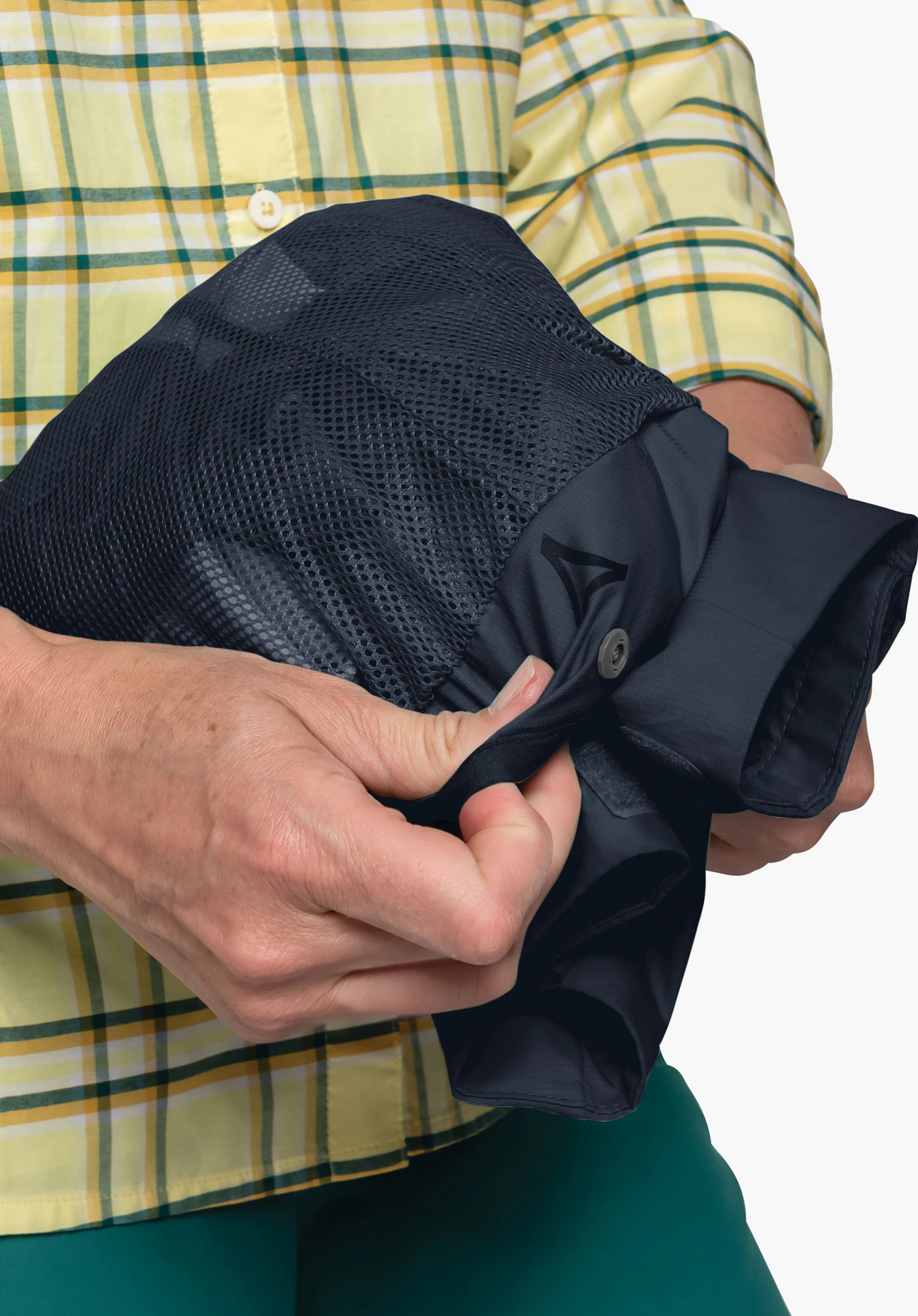 Jacket Easy XT L in blue, folded into the integrated mesh pocket, with a partially visible Schöffel logo and a press stud, held by two hands, close-up against a white/neutral background.